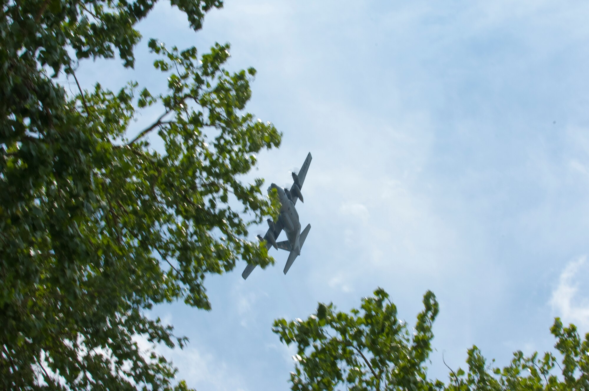 At a few hundred feet above ground, a C-130 "Hercules" banks over a tree and a crowd of friends and family on the Minnesota Air National Guard base on July 11, 2010 in a fly-by after returning from a tour in Afghanistan. The military cargo aircraft and about twenty Airmen are the first in a series of returns during July for the 133rd Airlift Wing in 2010. USAF official photo by Senior Master Sgt. Mark Moss