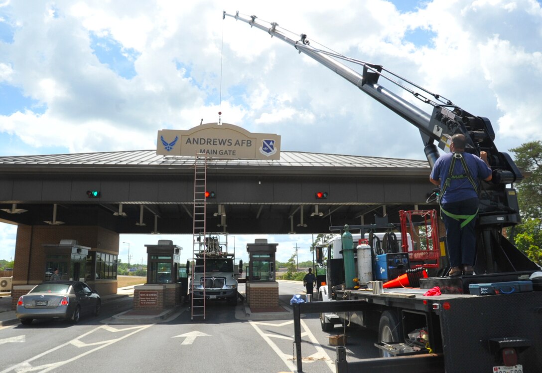 JOINT BASE ANDREWS, Md. -- A contracting agency uses a stationary crane to lower a new sign at the main entrance of Joint Base Andrews on Alabama Avenue July 9. The 18-foot - 4-foot sign is one of three signs which will also be mounted at the Virgina and Pearl Harbor Gate locations.  (U.S. Air Force photo by Bobby Jones)