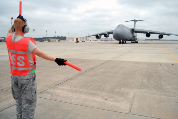 Senior Airman Michael DeNapoli, 43rd Aircraft Maintenance Squadron, marshals a C-5 to turn left toward for takeoff on the Pope flightline, July 13. Aircraft marshalling provides visual guidance between ground personnel and pilots on the aircraft. (U.S. Air Force Photo/ 1st Lt. Cammie Quinn) 