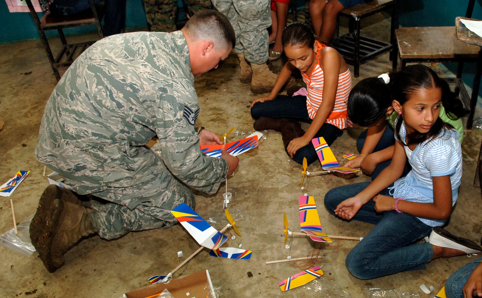Staff Sgt. Josh Lazarski, 820th Expeditionary RED HORSE Squadron, helps children assemble rubber band airplanes at the Sansonsito School July 12. (U.S. Air Force photo/Tech. Sgt. Eric Petosky)