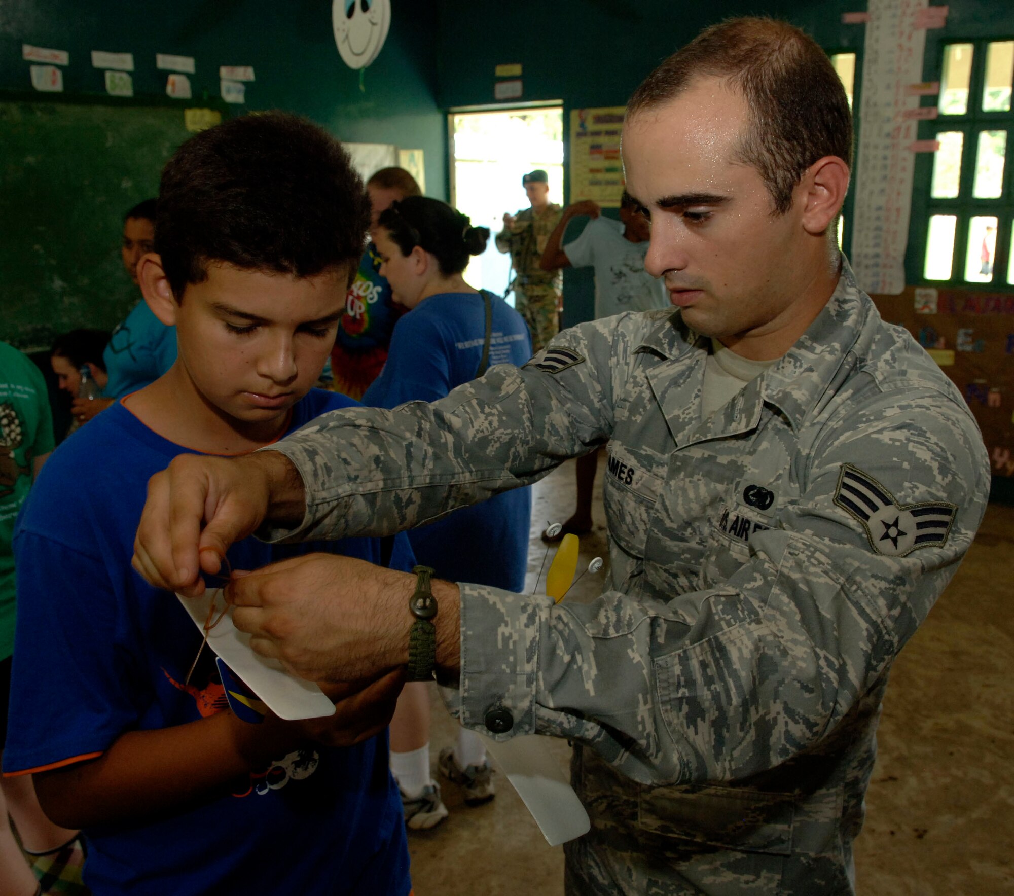 Senior Airman Alex James, 820th Expeditionary RED HORSE Squadron, helps children assemble rubber band airplanes at the Sansonsito School July 12. (U.S. Air Force photo/Tech. Sgt. Eric Petosky)