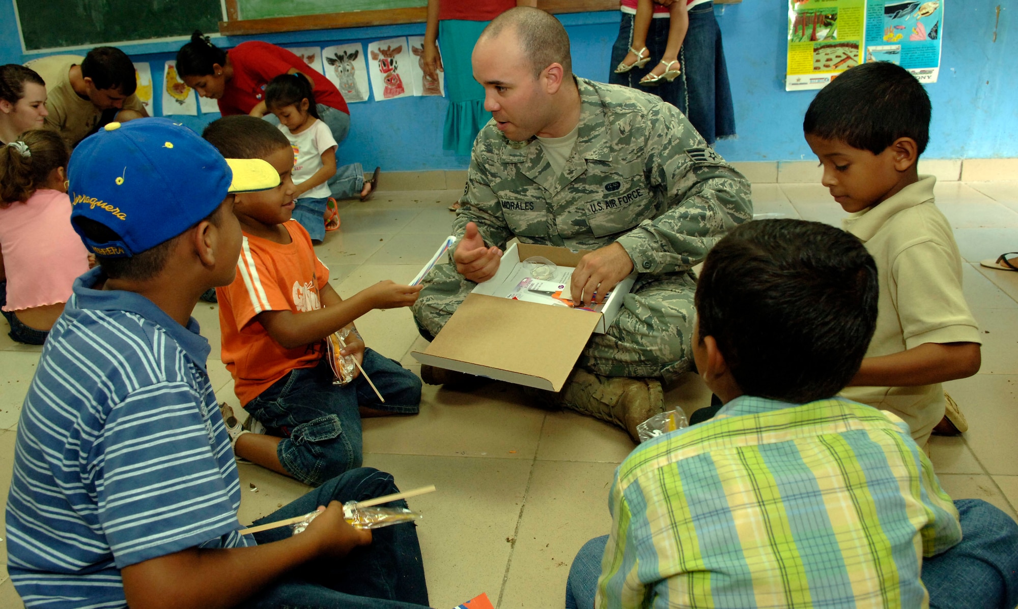 Senior Airman Cesar Morales, 820th Expeditionary RED HORSE Squadron, helps children assemble rubber band airplanes at the Sansonsito School July 12. (U.S. Air Force photo/Tech. Sgt. Eric Petosky)