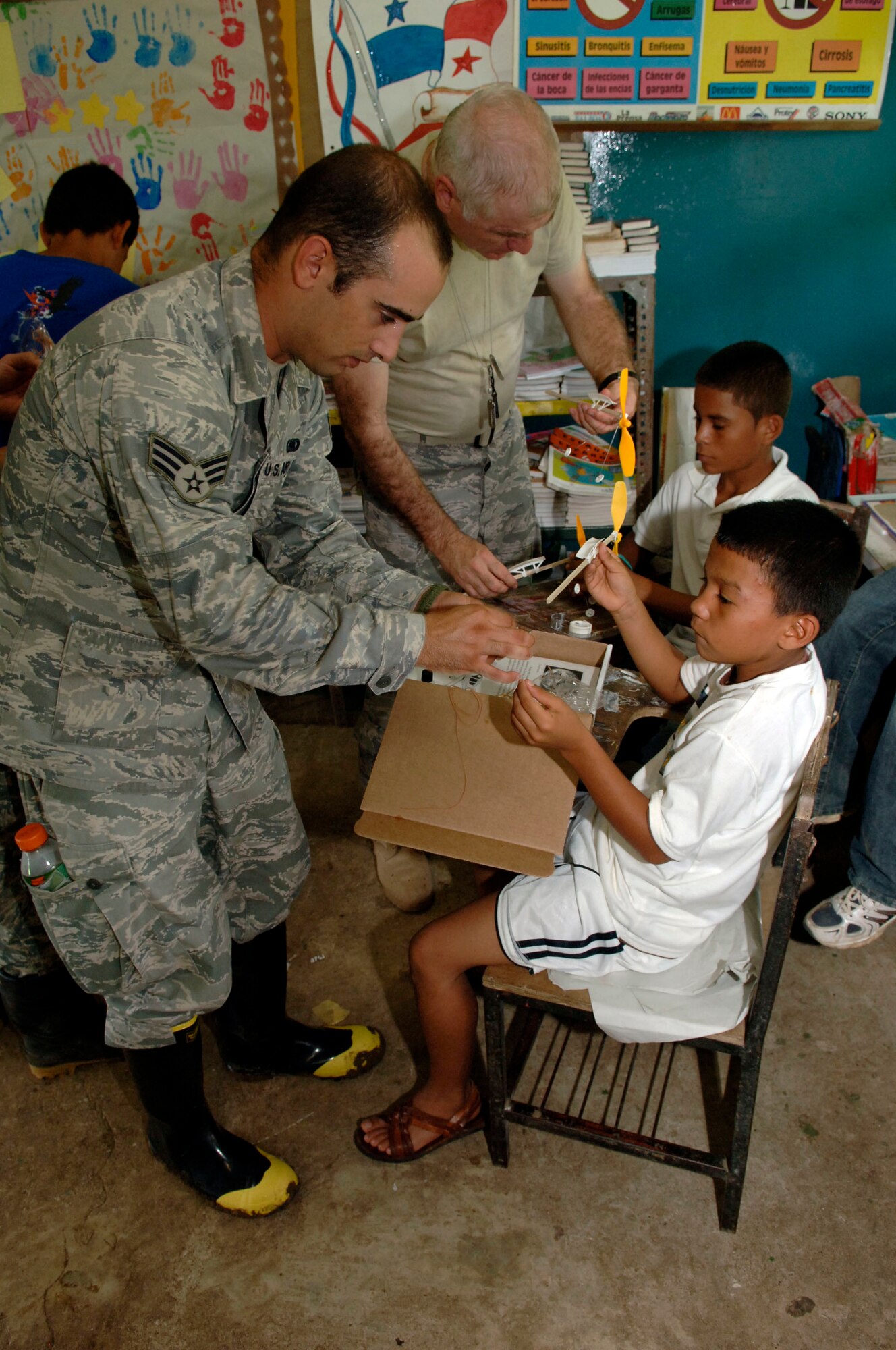 Senior Airman Alex James (left) and Maj. (Chaplain) Norris Burkes, 820th Expeditionary RED HORSE Squadron, help children assemble rubber band airplanes at the Sansonsito School July 12. (U.S. Air Force photo/Tech. Sgt. Eric Petosky)
