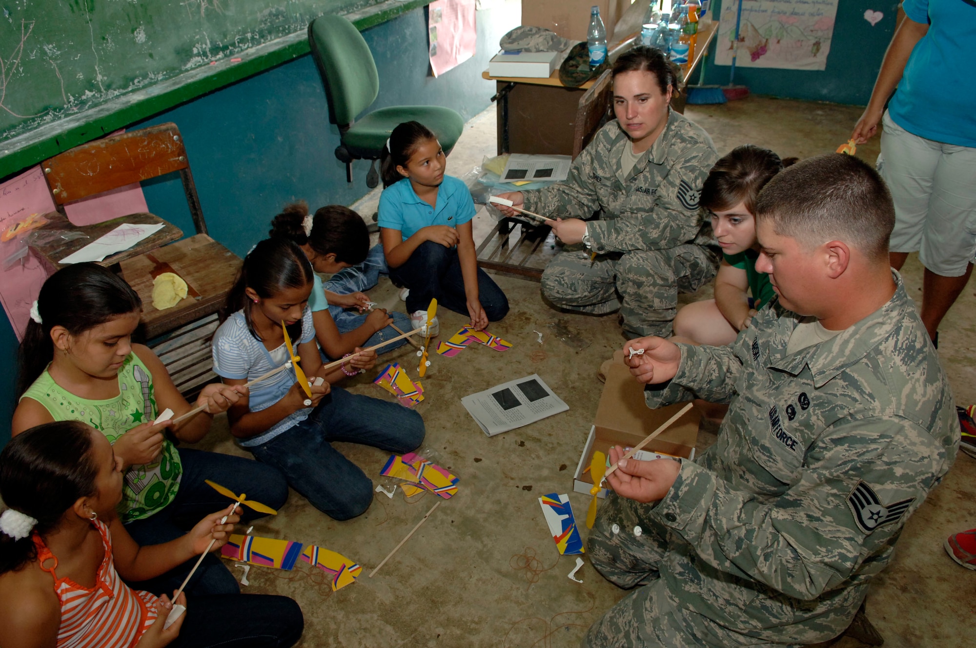 Tech. Sgt. Dorothy Lanthier and Staff Sgt. Josh Lazarski, 820th Expeditionary RED HORSE Squadron, help children assemble rubber band airplanes at the Sansonsito School July 12. (U.S. Air Force photo/Tech. Sgt. Eric Petosky)