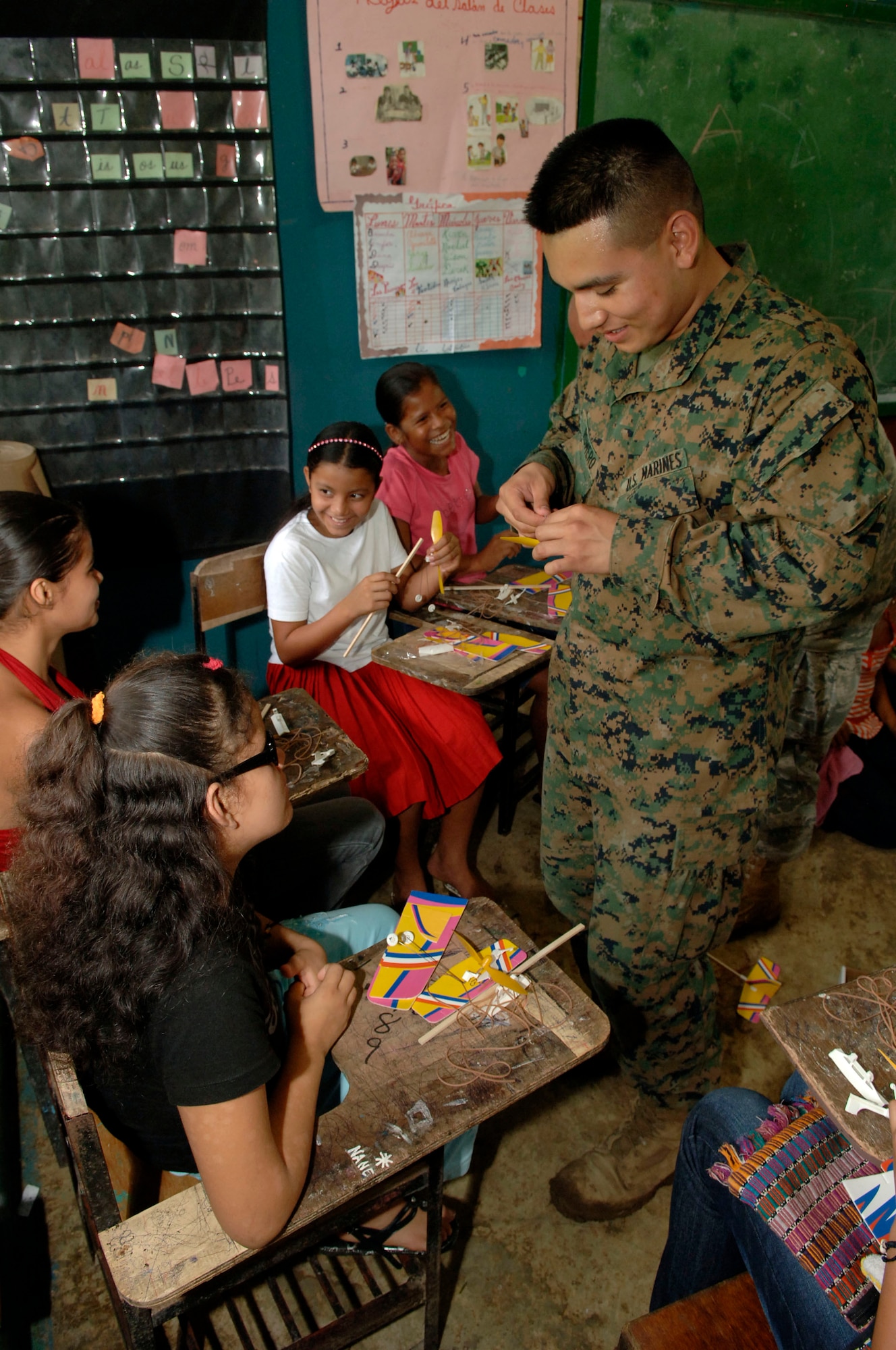 Pfc. Juan Romero, a civil affairs Marine deployed from the 4th Civil Affairs Group, helps children assemble rubber band airplanes at the Sansonsito School July 12. (U.S. Air Force photo/Tech. Sgt. Eric Petosky)