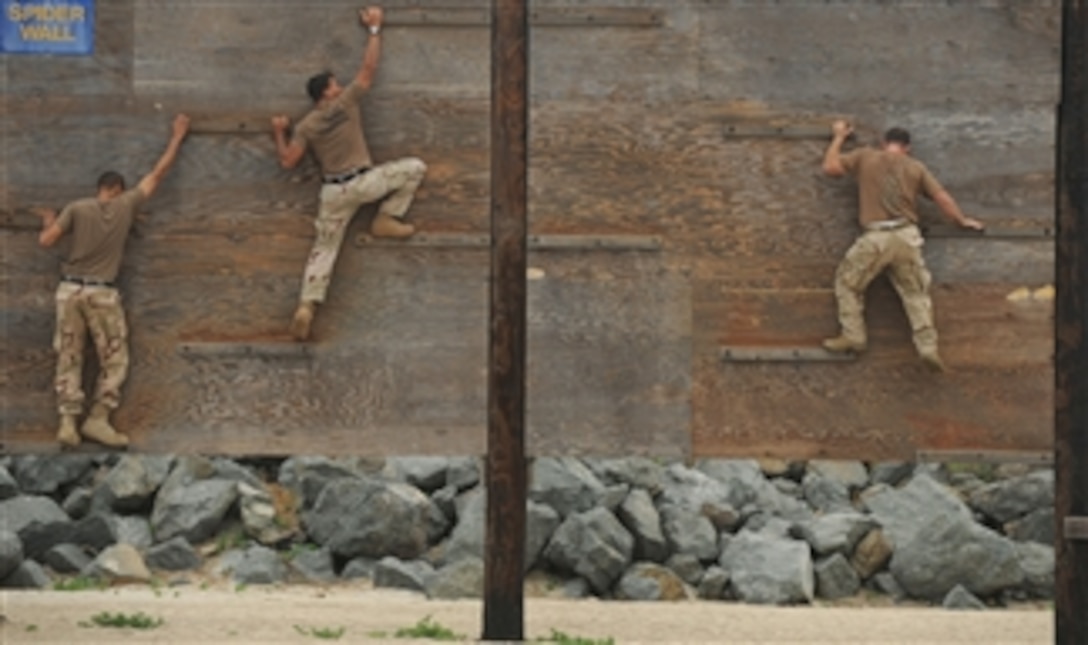 U.S. Navy Yeoman 2nd Class Keenan Leftridge (left), Petty Officer 1st Class Anderson Bomjardin and Chief Petty Officer Joseph Kane (right) climb up and over a portion of an obstacle course at the Naval Special Warfare Center in Coronado, Calif., on July 8, 2010.  The sailors, who are assigned to Fleet Combat Camera Group Pacific, navigate the obstacle course as part of physical training.  