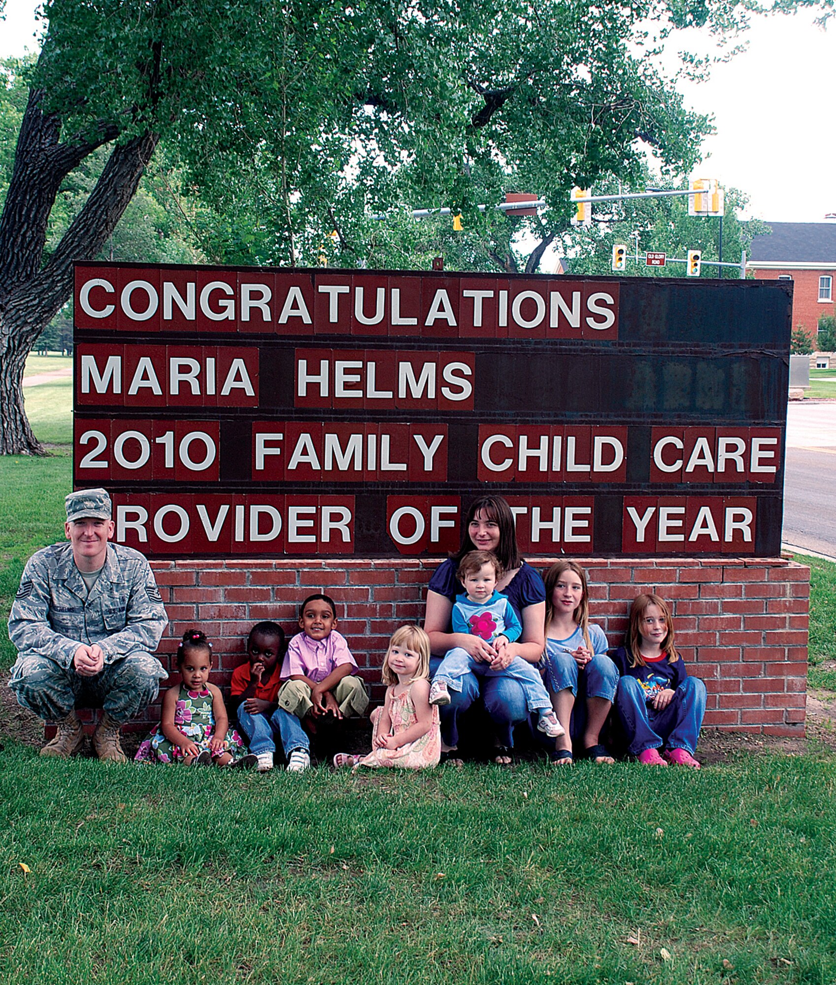 Maria Helms is the 2010 Family Child Care Provider of the Year. Tech. Sgt. Matthew Helms, 90th Medical Support Squadron, Neala Troia, Tavarius Pritchett, Dominic Troia, Megyn Helms, Skylar Kenko, Madyson Helms and Melyssa Helms pose  with Maria in front of a base marquee July 8. (U.S. Air Force photo by Airman 1st Class Jennifer Viveiros)
