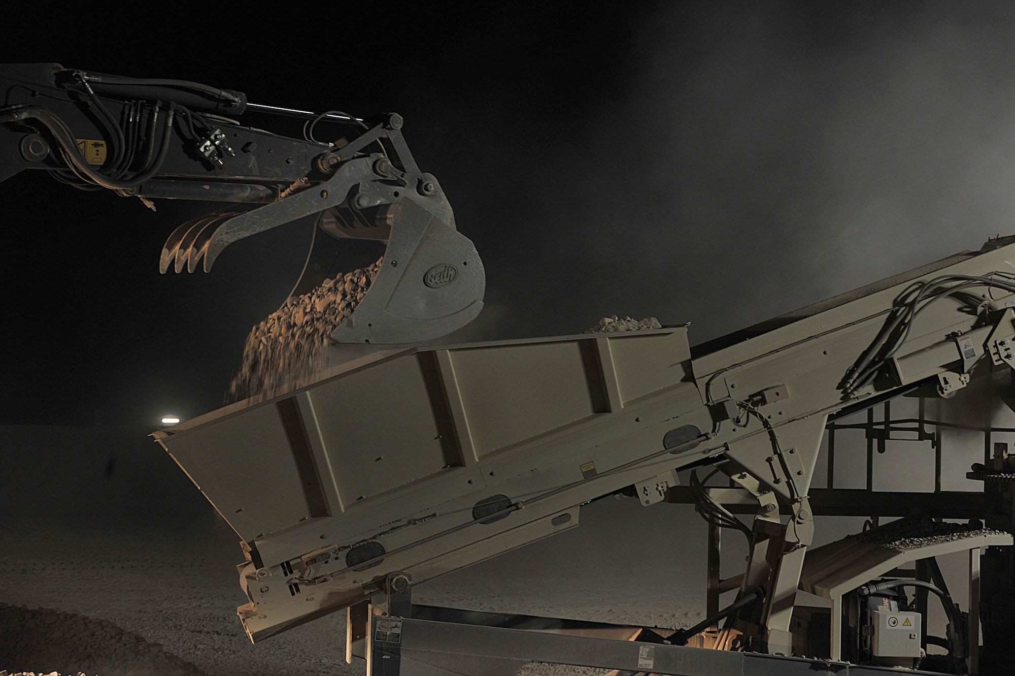 An excavator dumps rocks onto a conveyer belt to be crushed to make cement for a runway at Camp Dwyer, Afghanistan, June 24, 2010.  The runway will be used to accommodate heavier aircraft at Camp Dwyer.  (U.S. Air Force photo/Staff Sgt. Quinton Russ/released)