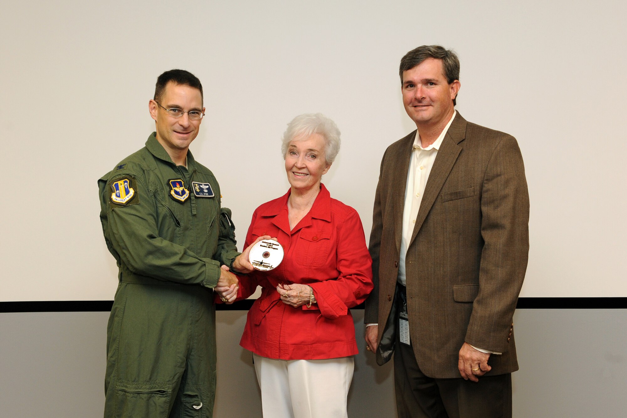 (Left) Col. Charles K. Hyde, 314th Airlift Wing commander, along with (right) Shane Evans, Lockheed-Martin Little Rock Air Force Base program manager, present a copy of their new C-130 360-degree training program July 15 to Joan Zumwalt, Jacksonville Museum of Military History chairman of the board and honorary 314th Airlift Wing vice commander. The C-130 program was donated to the Jacksonville Museum of Military History to help preserve present day history for the future. (U.S. Air Force photo by Senior Airman Ethan Morgan)