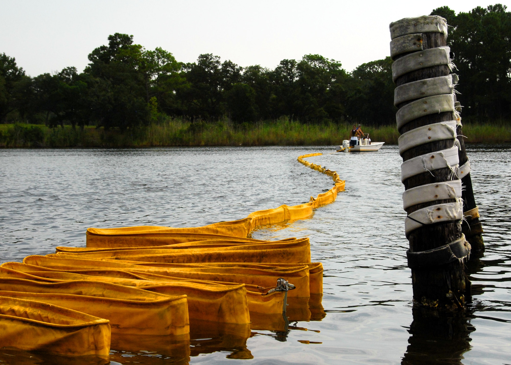 A boat begins to pull 300 feet of oil boom out into the waterway at Eglin Air Force Base, Fla., July 14.    Boom is an oil containment device used to trap oil in the water so it can be collected before reaching the shore.   Approximately 2,000 feet of booms have been installed around Eglin waterways.  (U.S. Air Force photo/Samuel King Jr.)