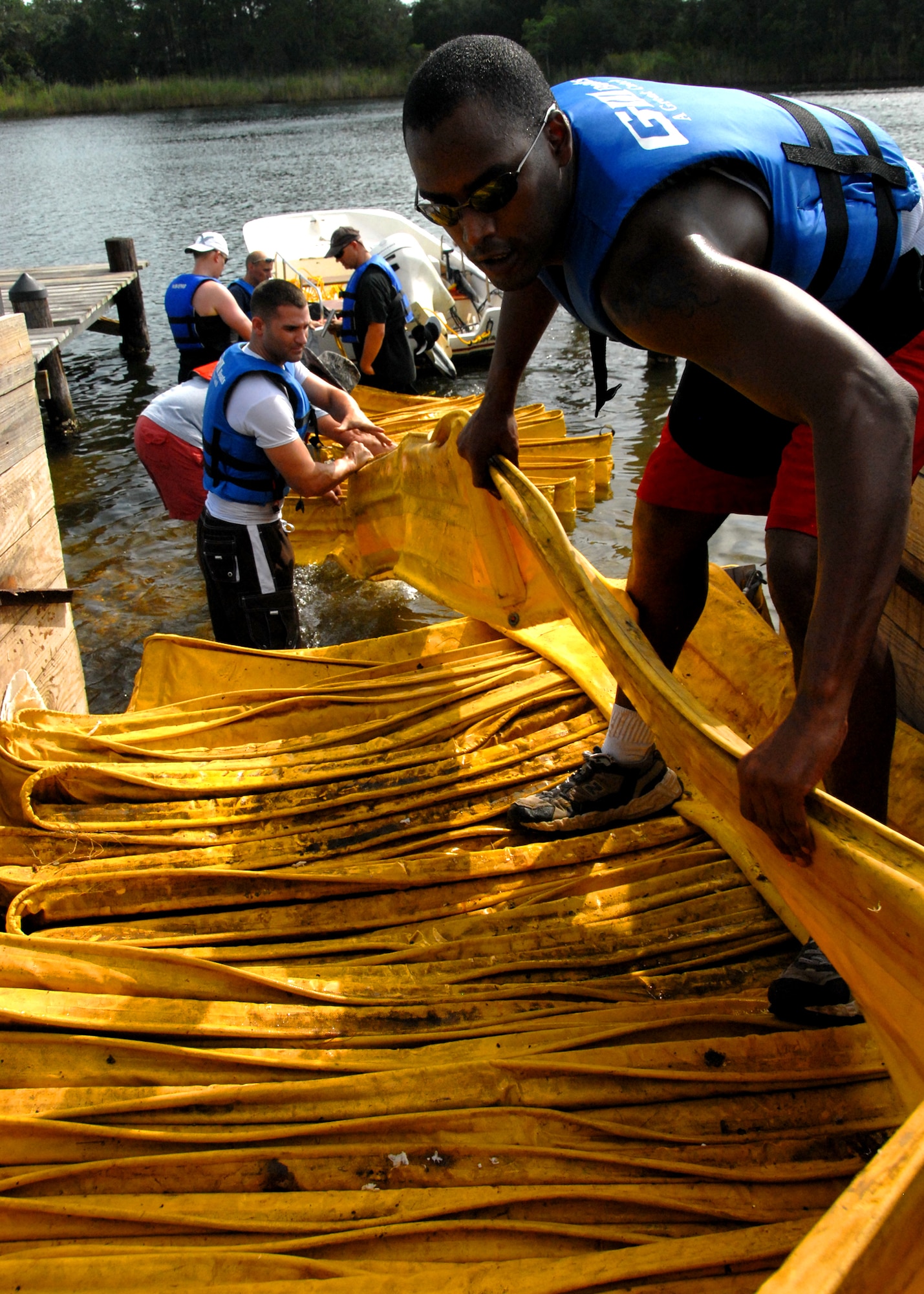 Staff Sgt. Adam Elerson (right) and Airman 1st Class Brian Beauchamp, 96th Aerospace Medicine Squadron, pull boom out of a trailer at Eglin Air Force Base, Fla.  600 feet of boom was taken to protect the shoreline July 14.  Boom is an oil containment device used to trap oil in the water so it can be collected before reaching the shore.   Approximately 2,000 feet of booms have been installed around Eglin waterways.  (U.S. Air Force photo/Samuel King Jr.)