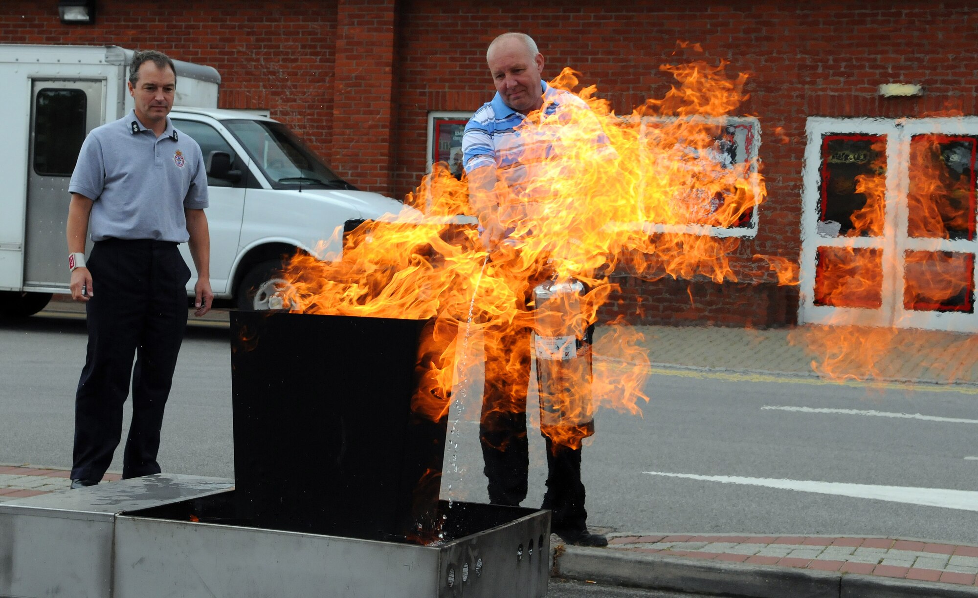 RAF MILDENHALL, England -- Clive Langford, a Base Exchange concessionaire, practices using a fire extinguisher while being observed by his instructor Adrian Delaney, RAF Mildenhall Fire Department watch manager, outside the BX July 15. The fire department taught concessionaires from RAFs Mildenhall and Lakenheath to use the PASS method to put out small fires when it is safe to do so. This technique involves pulling the extinguisher pin, aiming at the base of the fire, squeezing the extinguisher handle and sweeping from side to side until the fire is out. (U.S. Air Force photo/Staff Sgt. Thomas Trower)