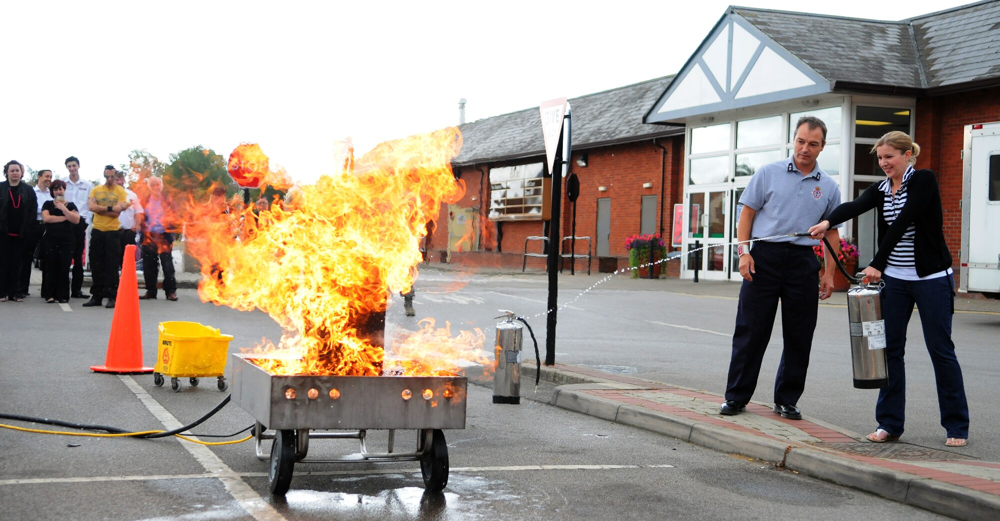 RAF MILDENHALL, England -- Ela Toombs, a Base Exchange concessionaire, practices using a fire extinguisher while being observed by her instructor, Adrian Delaney, RAF Mildenhall Fire Department watch manager, outside the BX July 15. The fire department taught concessionaires from RAFs Mildenhall and Lakenheath to use the PASS method to put out small fires when it is safe to do so. This technique involves pulling the extinguisher pin, aiming at the base of the fire, squeezing the extinguisher handle and sweeping from side to side until the fire is out. (U.S. Air Force photo/Staff Sgt. Thomas Trower)
