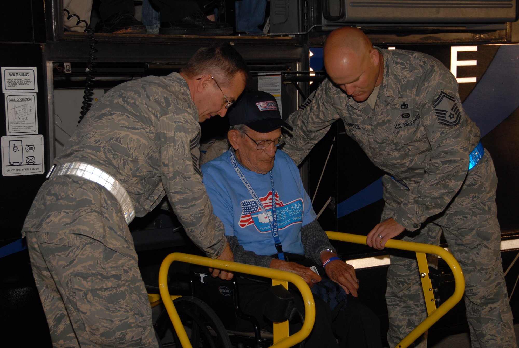 Senior Master Sgt. Stephen Rosebrook and Chief Master Sgt. Steven Keene, both assigned to the 137th Logistics Readiness Squadron, help a veteran onto an airplane on the base flight line.  Veterans who were wheelchair bound were given the royal treatment as they were lifted off the bus and carried onto the charted flight to Washington, D.C. and the World War II Memorial.
