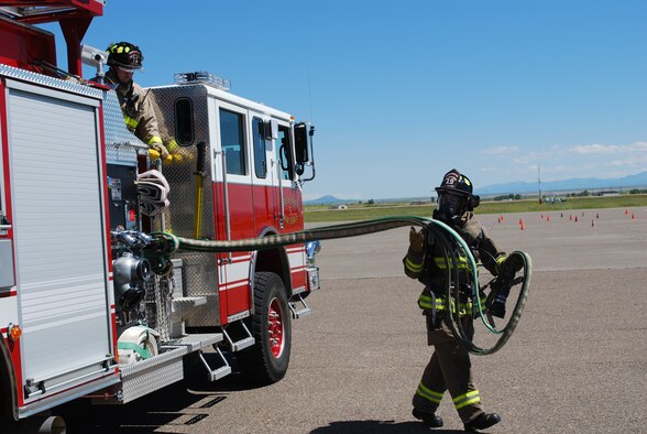 Airman 1st Class Nathan Johnson, 341st Civil Engineering Squadron firefighter, deploys a hand line from a fire engine during training at the base fire department July 8. Airman 1st Class Mark Martin, 341st CES firefighter, monitors area safety from inside the vehicle. (U.S. Air Force photo/Airman 1st Class Kristina Overton)