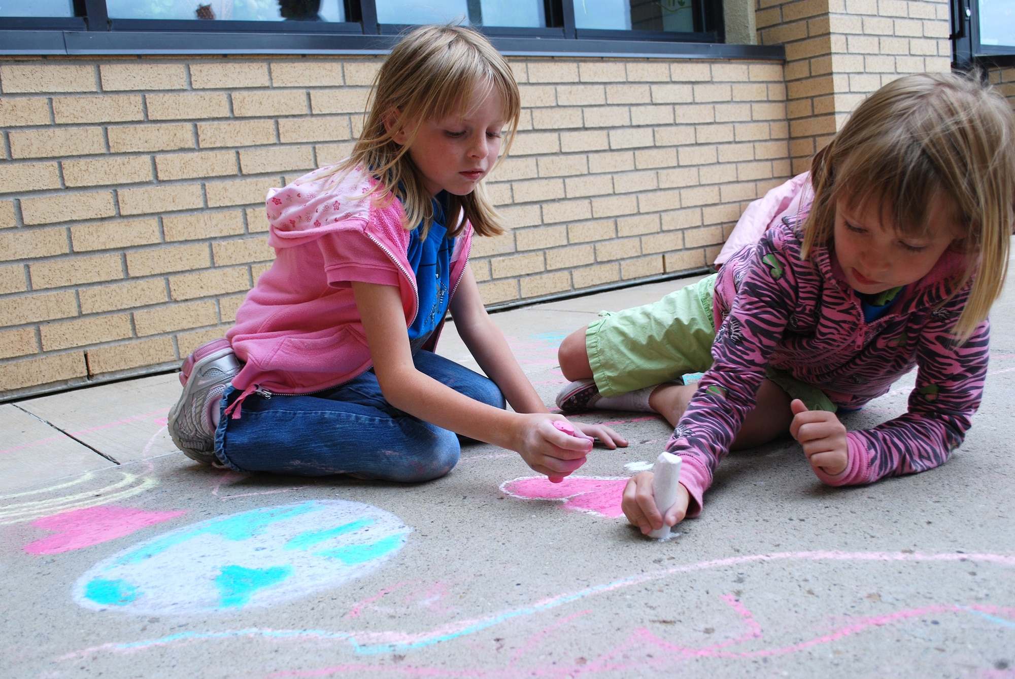 Little Warriors Kaitlyn, 6, and Hailey, 7, place the finishing touches on their “Mother Earth” themed chalk artwork right outside of the Youth Center entrance. (U.S. Air Force photo/Airman 1st Class Kristina Overton) 