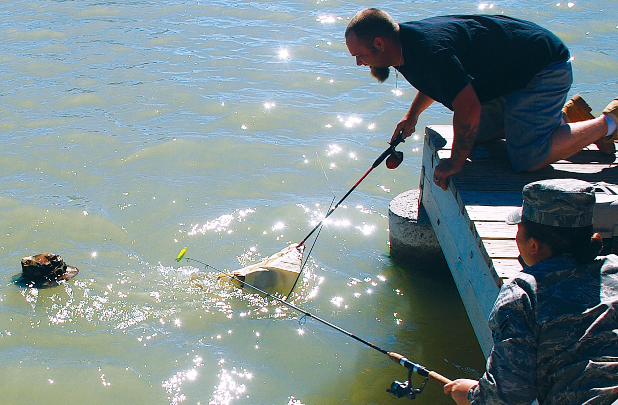 Jon Myers and Airman 1st Class Jennifer Dowling, 90th Civil Engineer Squadron, try to fish a veteran’s hat and bag out of the water during the disabled veterans fishing day held at the base lakes on July 16. (U.S. Air Force photo by Staff Sgt. Mike Tryon)