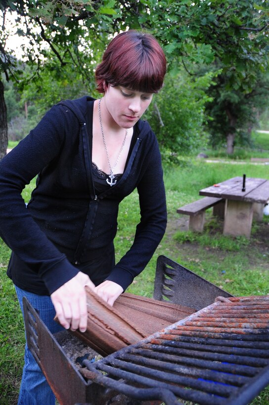 ELLSWORTH AIR FORCE BASE, S.D. -- Airman Megan Dix, Air Force Financial Services Center travel technician, arranges fire logs in a camp grill at Spring Creek, S.D., July 22.  Airman Dix ensures all the logs are safely contained within the grill. (U.S Air Force photo/Airman 1st Class Anthony Sanchelli)