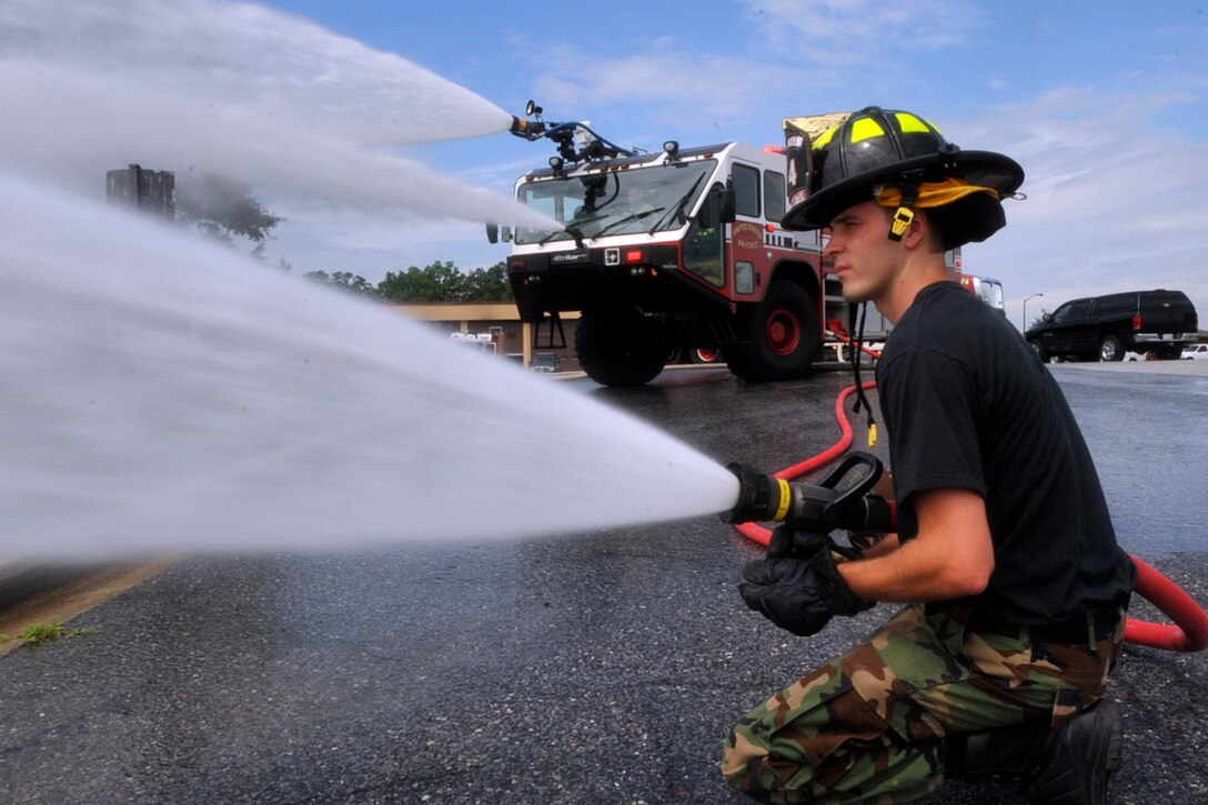 JOINT BASE ANDREWS, Md. -- Senior Airman Shawn Suber, 316th Civil Engineer Squadron firefighter, discharges a fire hose as a fellow squadron member, Senior Airman Jason Holmes (inside a Station P-19 Striker truck) disperses water from top and bottom water turrets during flightline aircraft crash simulation training July 21 here.  (U.S. Air Force photo by Bobby Jones)
