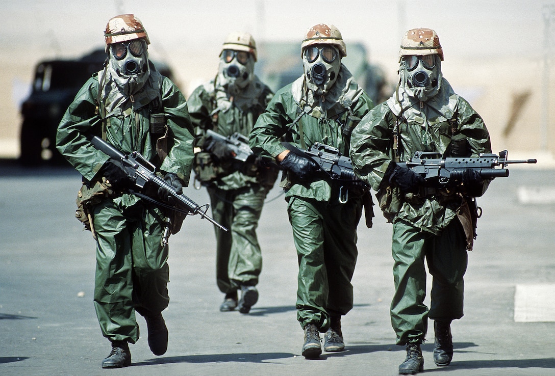 Four soldiers from the 82nd Airborne Division walk around their camp wearing rain suits, gloves and M-17A1 protective masks as they try to acclimate their bodies to the heat of the Saudi summer during Operation Desert Shield.