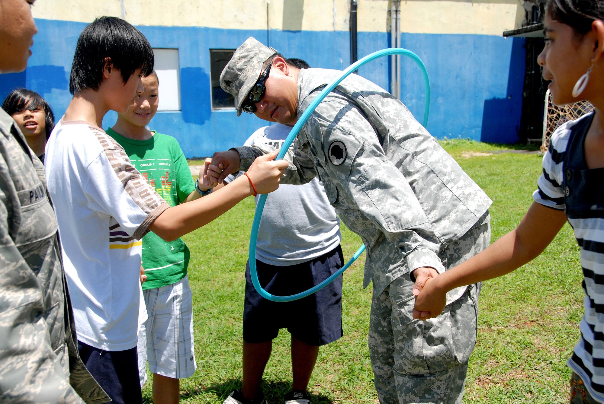 Sgt. Isaac Norita, Counterdrug, Hawaii Army National Guard, works his way through Hula Hoop as middle school students try to get through the Hula Hoop without touching it or breaking the human chain. Air and Army National Guard Counterdrug personnel from Hawaii and Idaho joined the Guam Counterdrug Demand Drug Reduction program at V.S.A. Benavente Middle School on Guam, June 29. The Counterdrug personnel put the students through a serious of exercises designed to develop teamwork and communication. (U.S. Air Force photo/Tech. Sgt. Betty J. Squatrito-Martin)