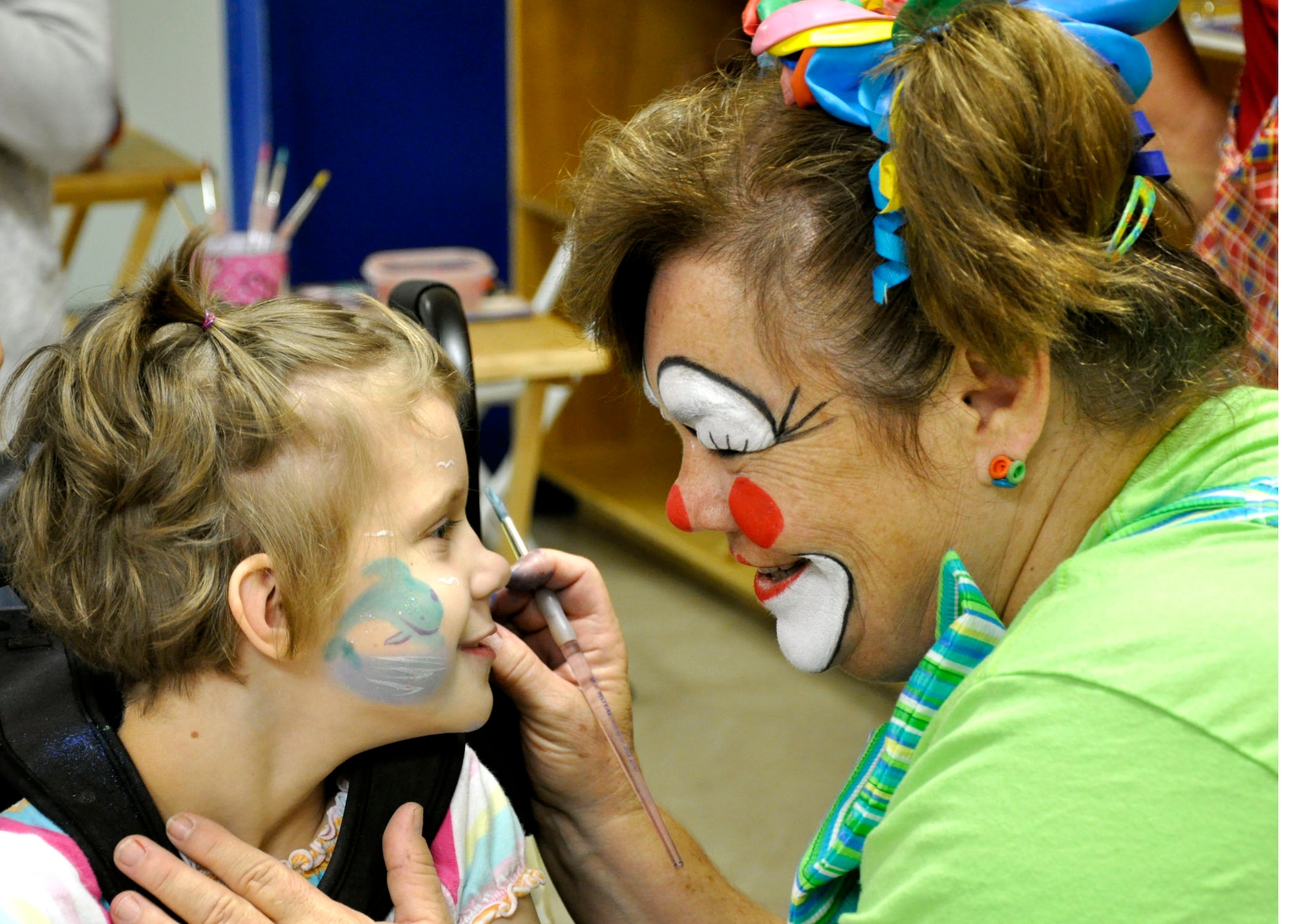 “Giggles” the clown, paints a dolphin on Lili Sparks, age 8, at the Kids Day event at the Youth Center, July 24.  The Youth Center and Airman and Family Readiness Center coordinated the event for family members enrolled in the Exceptional Family Member’s Program. The event was designed as a day camp for members and their families. (U.S. Air Force photo/ Errica Bennett)