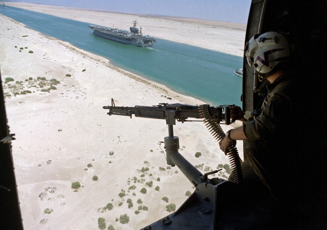 A gunner in a Helicopter Anti-submarine Squadron 5 SH-3H Sea King helicopter mans an M-60 machine gun as the nuclear-powered aircraft carrier USS Eisenhower transits the Suez Canal below following a deployment in support of Operation Desert Shield.