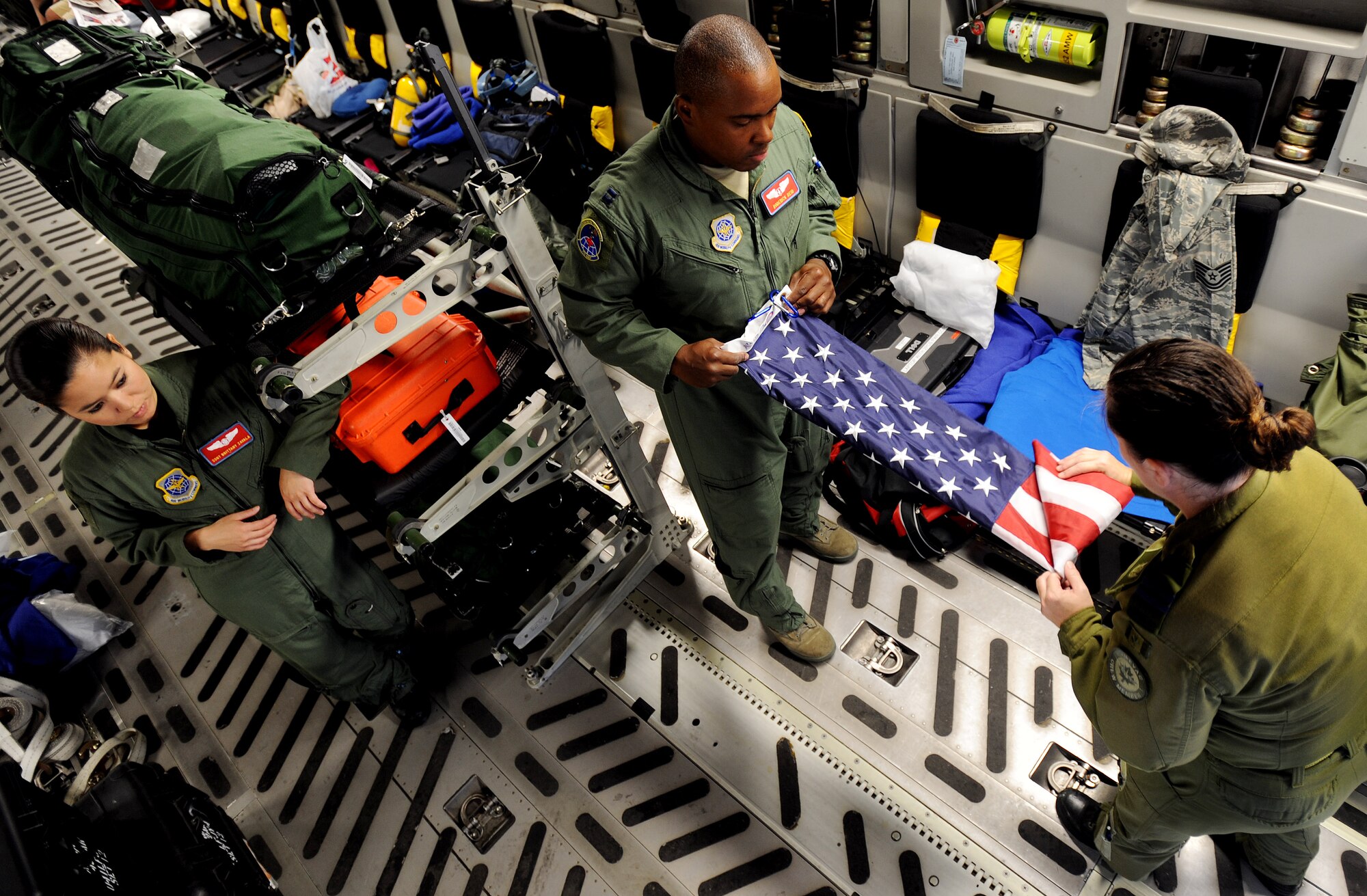 Captains Roderick Reid, center, and Carol Nicholson, flight nurses from the 775th Expeditionary Aeromedical Evacuation Flight, fold an American flag on a C-17 Globemaster III aircraft at Naval Air Station North Island, Calif., as Staff Sgt. Brittany Zavala, a 775 EAES aeromedical evacuation technician watches, during the weekly Integrated ICMOP mission. Capt. Nicholson, a dual qualified flight nurse for the Canadian and U.S. Air Forces who is participating in an exchange program, says the flag belongs to her and she always flys it during the ICMOP. “It means a lot to me to fly the flag and brings a tear to my eye to see it flying over the cargo area when there are wounded Americans onboard.”  (U.S. Air Force photo by Master Sgt. Rick Sforza)