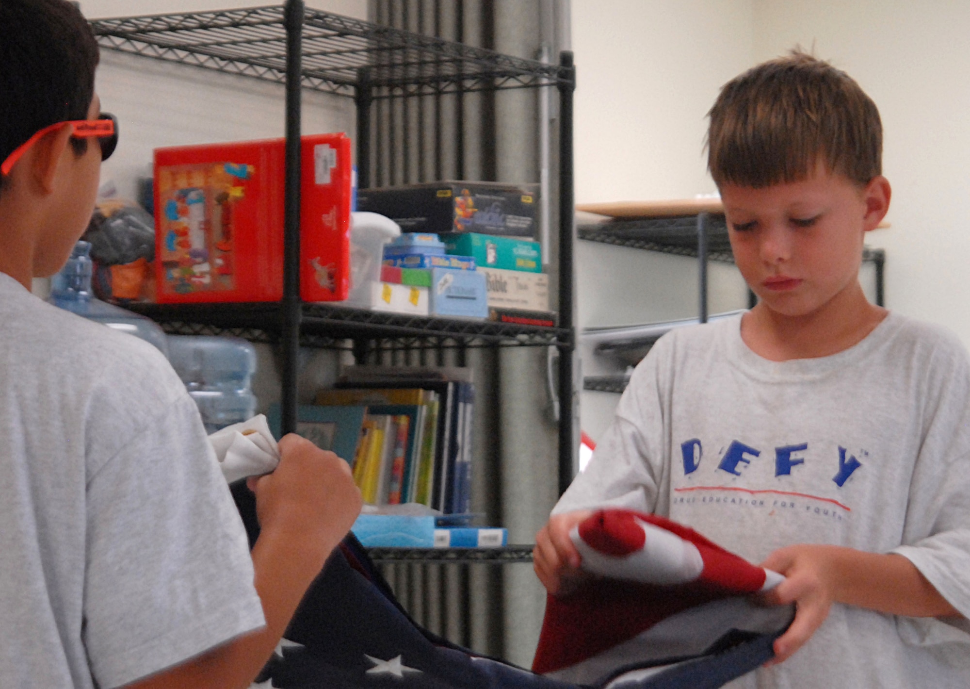 Chris Shaffer folds the American flag at the start of the day for DEFY camp July 27 with the help of Jaden Hendrix. Along with learning how to resist drugs, alcohol and peer pressure to join gangs, DEFY camp participants also learned flag protocol. (U.S. Air Force photo/Connie Hempel)