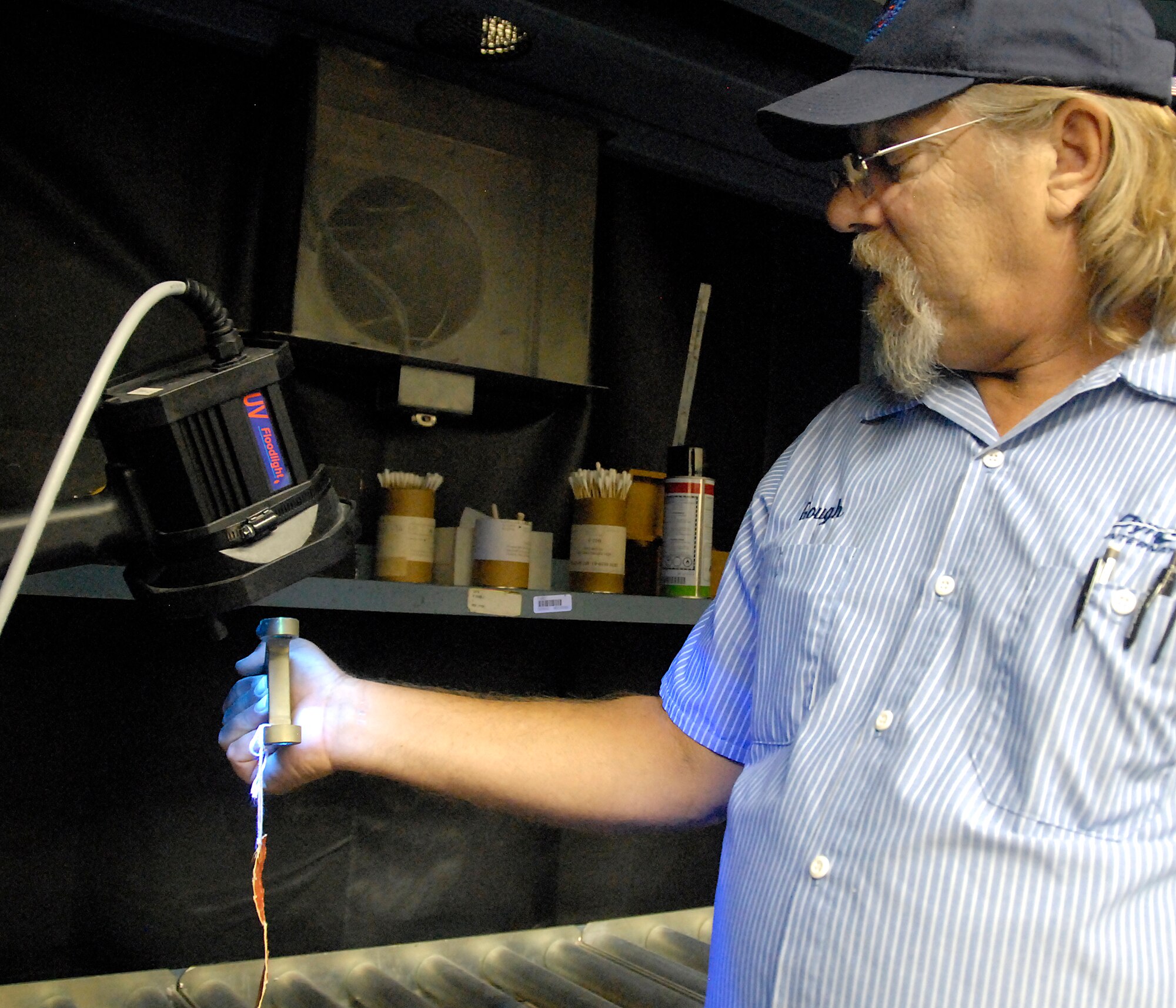 Don Gough, the lead specialist at the 80th Flying Training Wing's Non-destructive Inspection shop, looks at an aircraft part under a black light July 26 to look for defects. The fluorescent penetrate is one of five techniques used by specialists to search for cracks or other defects in aircraft parts or airframes. The shop also uses ultrasound, magnetic particle, eddy current and X-ray. (U.S. Air Force photo/Mike Litteken