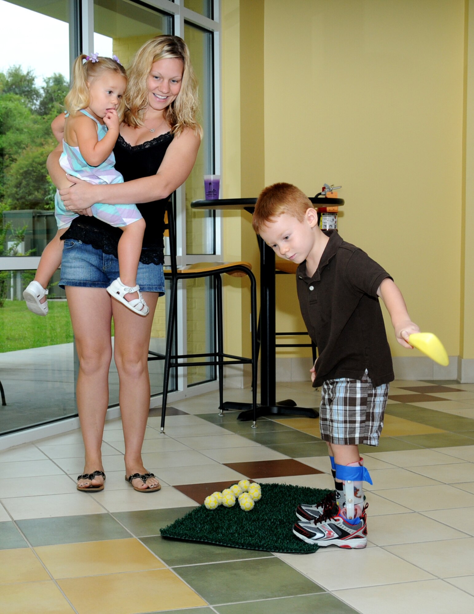 Christine Williams holds her 2-year-old daughter, Kylee, as her 4-year-old son, Cadden, practices his putting skills.  Their dad, Navy Construction Mechanic 2nd Class Donald Williams, is deployed.  (U.S. Air Force photo by Kemberly Groue)
