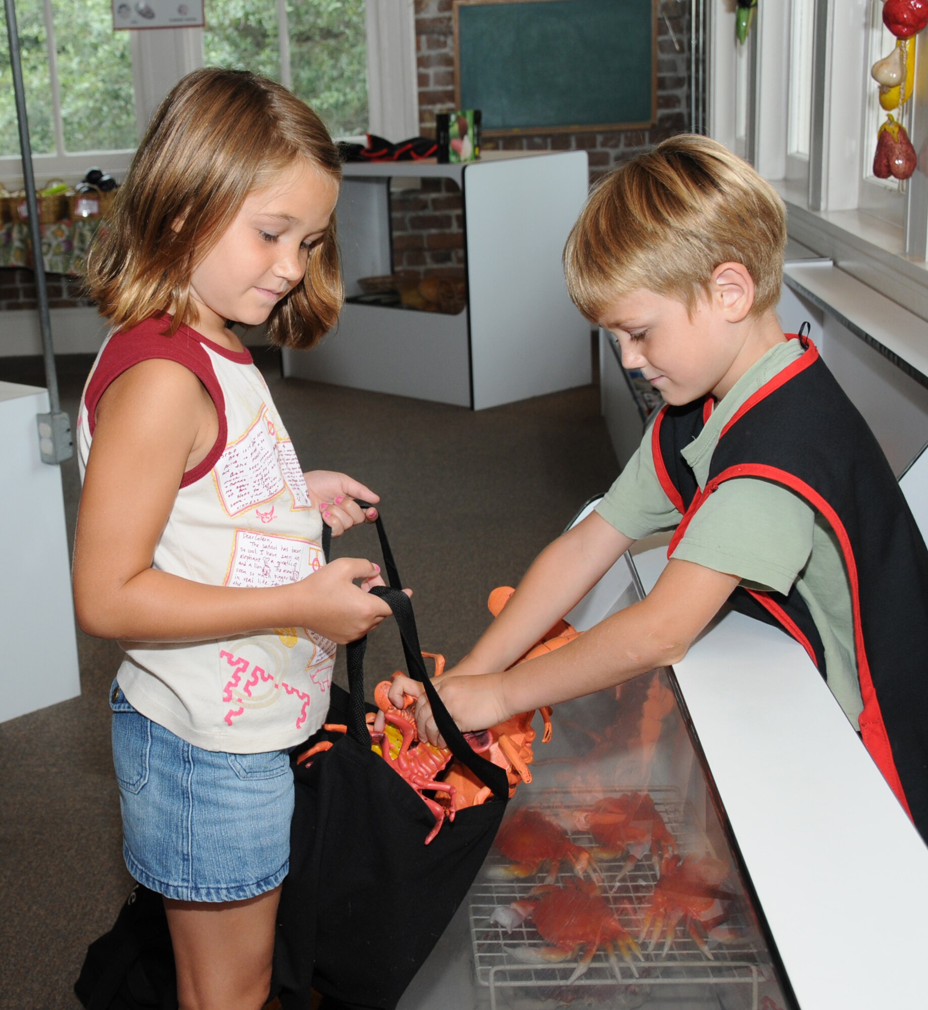 Annie Cook, 8, makes a seafood purchase from her 6-year-old brother, John, at the grocery store play area.  Their parents are Navy Lt. Cmdr. Dan and Emily Cook. Their father is deployed.  (U.S. Air Force photo by Kemberly Groue)