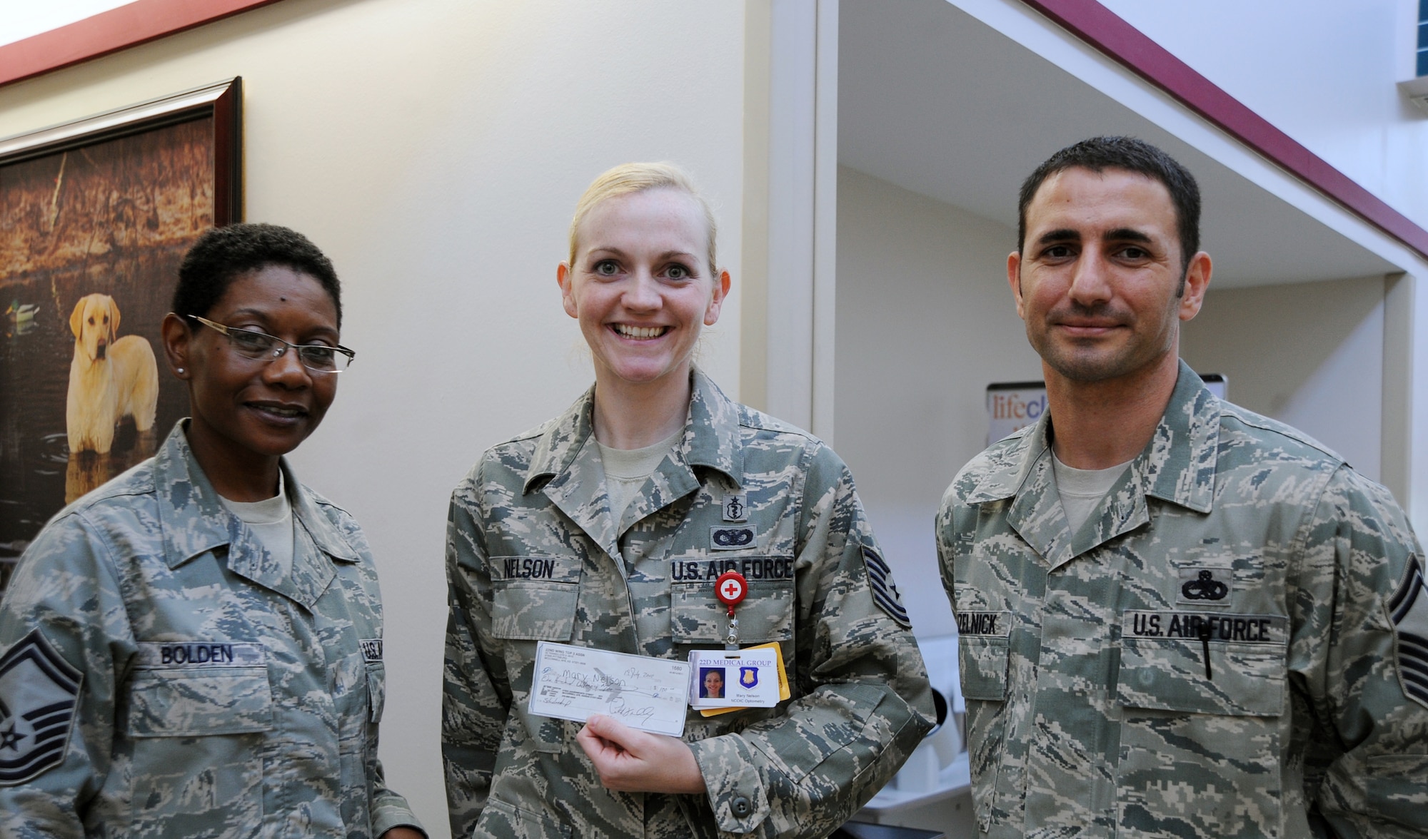 Senior Master Sgt. Vivian Bolden, left, 22nd Force Support Squadron professional development coordinator and Top 3 president, and Senior Master Sgt. Brian Kruzelnick, right, 22nd Aircraft Maintenance Squadron aircraft maintenance unit assistant superintendent and Top 3 vice president, present Tech. Sgt. Mary Nelson, 22nd Aerospace Medical Group optometry clinic NCO, a check for $100.  Sergeant Nelson was chosen as the winner because of her quality of writing for this quarter’s essay topic, “If you are non-deployable, should you be able to stay in the Air Force?”  The scholarship is presented each quarter to the winner of the essay contest and is open to all active-duty military, grades E-1 through E-6.  (U.S. Air Force photo illustration/Airman 1st Class Andrea Salazar)
