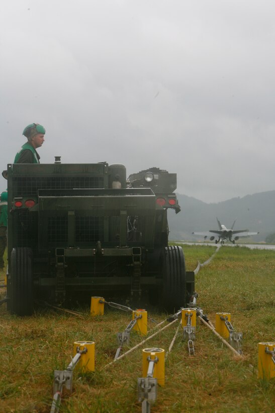 A recovery Marine prepares to retract the deck pendant after a successful arrestment during exercise Invincible Spirit here July 28. During retraction, arrestment gear operators on either side of the runway must act together to properly pull back the arrested plane to release the deck pin from the tail hook.