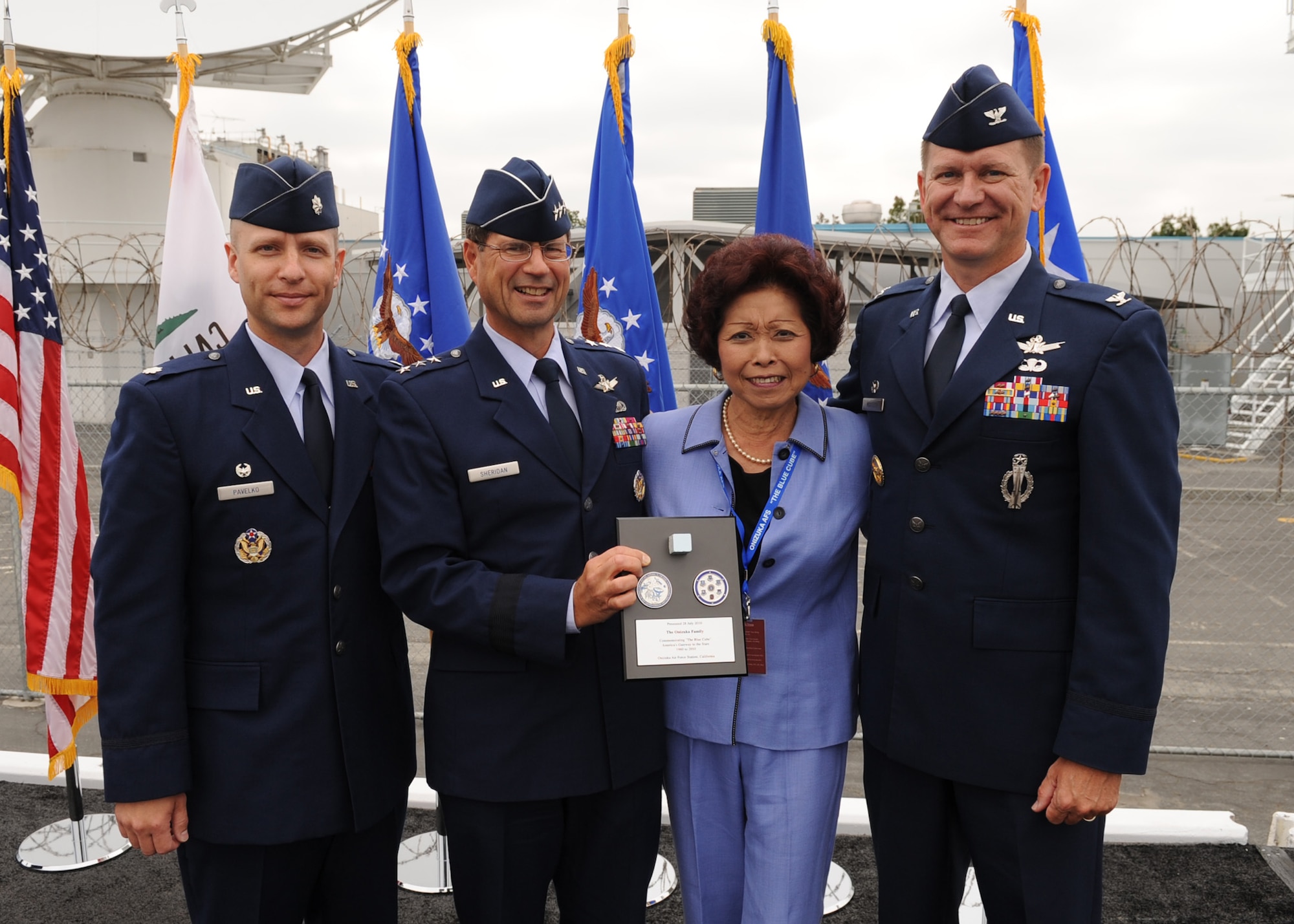 SUNNYVALE, Calif.-- Lt. Gen. John T. Sheridan, commander of the Space and Missile Center, Los Angeles Air Force Base, Col. Wayne Monteith, the 50th Space Wing commander, and Lt. Col. Robert Pavelko, 21st Space Operations Squadron commander, present a commemorative plaque here Wednesday, July 28, 2010 to Lorna Onizuka, widow of Col. Ellison Onizuka, astronaut aboard the Space Shuttle Challenger disaster. Built in 1960, Onizuka AFS was originally known as the Air Force Satellite Test Center. It was selected for closure by the Base Closure and Realignment Commission in 2005, with the recommendation to move operations to Vandenberg Air Force Base, in order to consolidate satellite command and control operations while reducing excess infrastructure.  (U.S. Air Force Photo/Senior Airman Bryan Boyette)