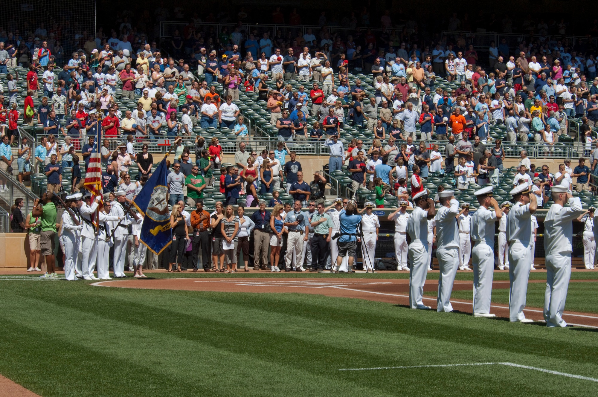 U. S. Navy Reserve Sailors based in Minnesota stand along the baselines while an honor guard presents the colors during the national anthem at the beginning of a Minnesota Twins game at Target Field on July 21, 2010. Overhead, after jumping out of a 133rd Airlift Wing C-130, the U. S. Navy parachute team "Leap Frogs" trail smoke and bring the game ball. The Minnesota Twins are celebrating Navy Day in their new stadium. The Air National Guard crew is joined by aviators from the 934th Airlift Wing, U. S. Air Force Reserve supporting this event.  USAF official photo by Senior Master Sgt. Mark Moss