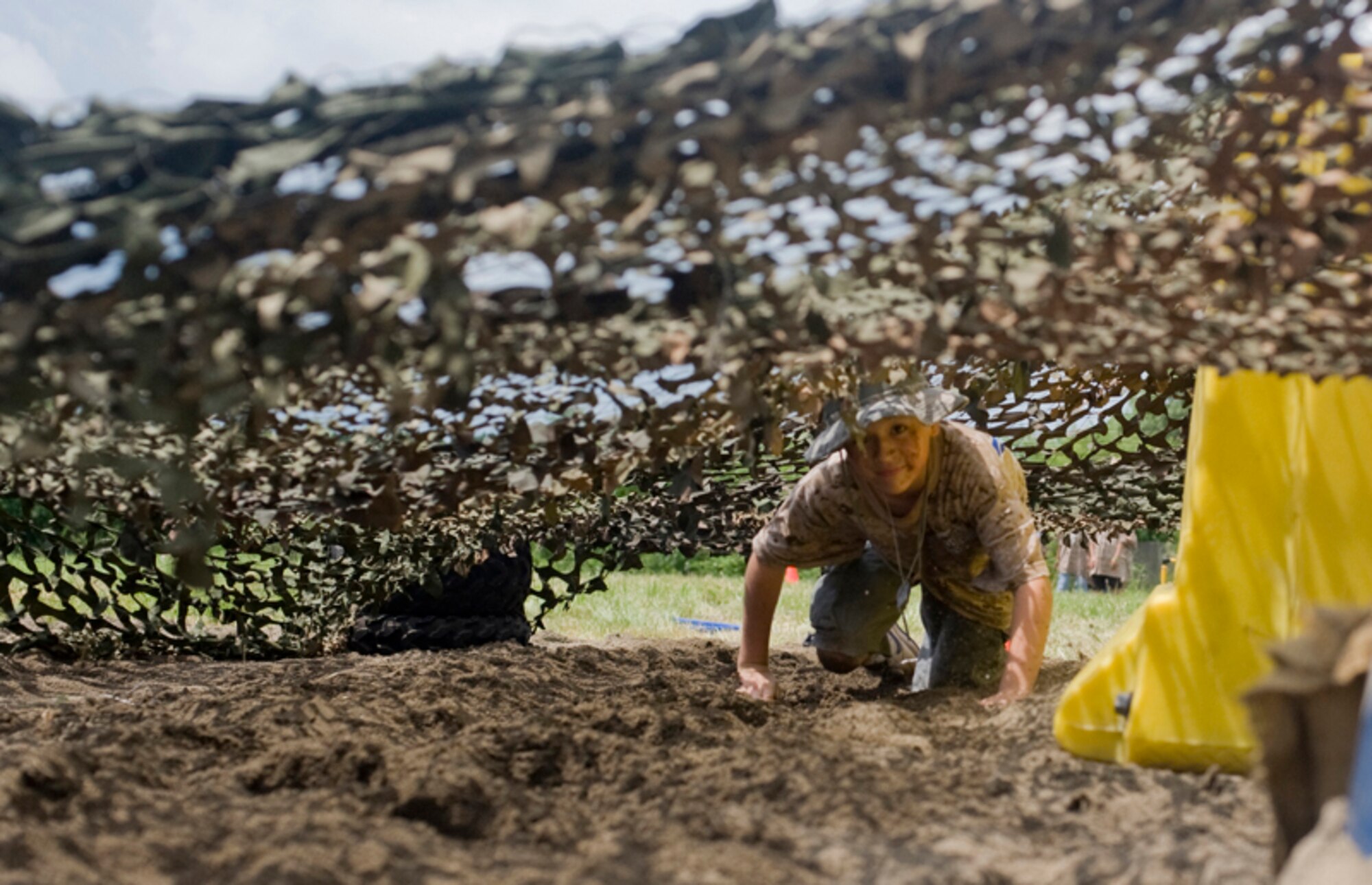 Albert Robinson, 10, son of Staff Sgt. Shilo Whit Hawk, low crawls under camouflage netting, July 24, during Misawa’s first Operation Children on Deployment Exercise. After receiving dog tags and deployment orders, about 180 military children processing through a mobility line. They experienced pre-deployment training and departed to Camp Defender to get an idea of what it’s like when their parents deploy.  (U.S. Air Force photo/ Senior Airman Jessica Lockoski)