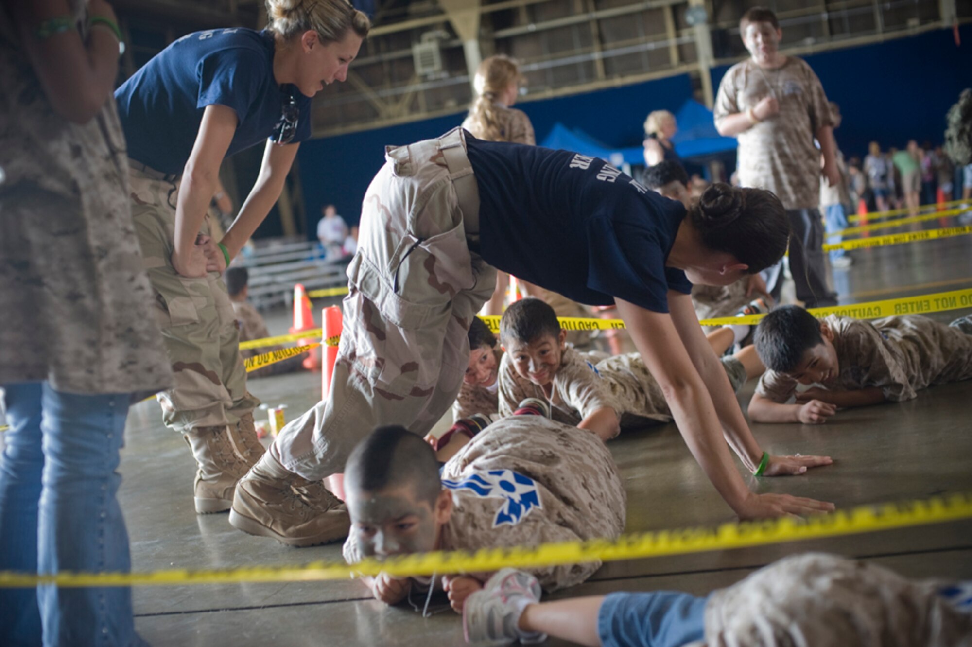 Staff Sgt. Kristen Joiner encourages military children to low crawl under Senior Airman Laura Yager, July 24, during Misawa’s first Operation Children on Deployment Exercise. The Airmen volunteered as military training leaders who lead one of several groups of children through military training activities during Operation CODE.  (U.S. Air Force photo/ Senior Airman Jessica Lockoski)