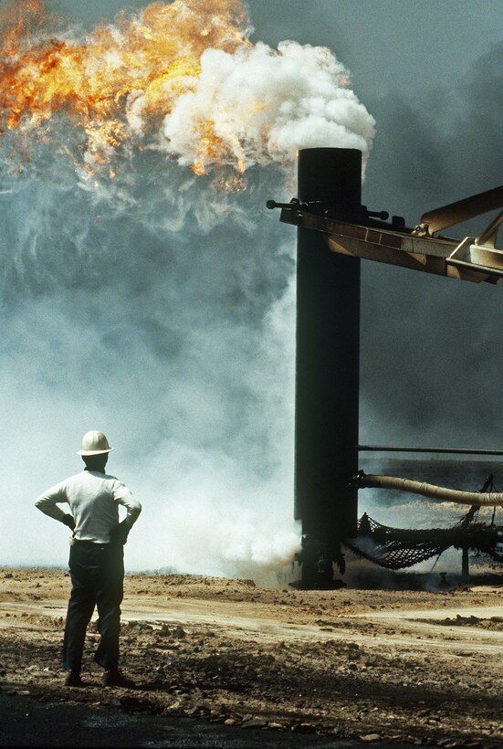 Firefighters from the Boots and Coots Oil Well Firefighting Company use a crane to cap a blazing well in the aftermath of Operation Desert Storm.  The well, situated in the Ahman Oil Fields, is one of many set afire by Iraqi forces prior to their retreat from Kuwait.