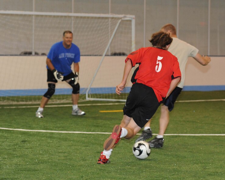 Nicholas M. Reynolds (red shirt), 319th Civil Engineer Squadron, advances the ball toward the goal, which is tended by Col. Don Shaffer (blue shirt), 319th Air Refueling Wing commander, during a soccer tournament July 28 at the Grand Forks Air Force Base Fitness Center.  The tournament was held after an official ribbon cutting ceremony for the fitness center’s new turf surface. The 319th Maintenance Group beat the 319th CES 4-3 in the championship game. (U.S. Air Force photo by Airman 1st Class Amber Price)