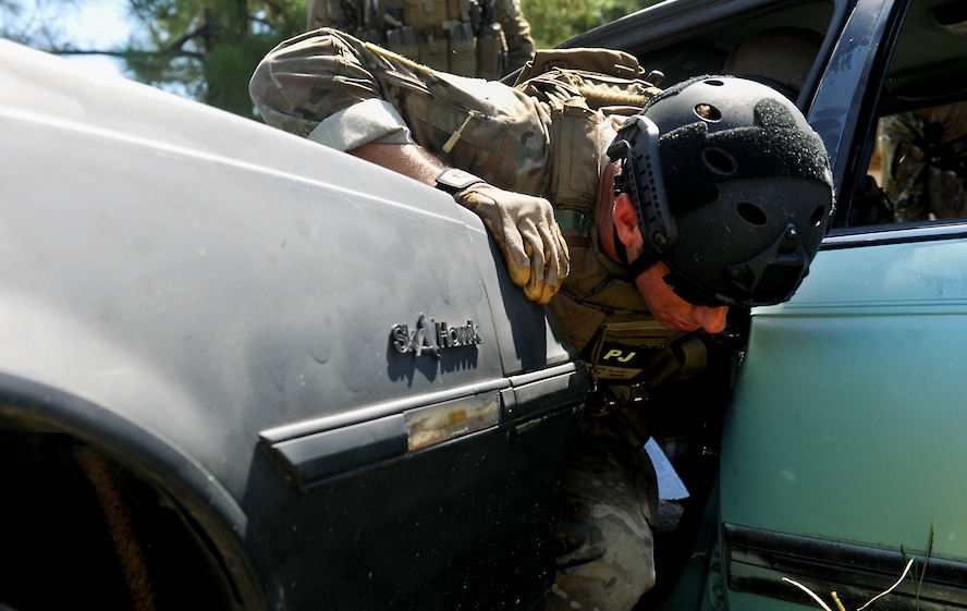 VALDOSTA, Ga. -- Senior Airman Trevor Clark, 38th Rescue Squadron pararescueman from Moody Air Force Base, Ga., climbs through a front door and in between two vehicles during a confined spaces exercise at a local junkyard here July 27. Airman Clark maneuvered through one car, broke through the window and slid in between two vehicles in order to gain access to another vehicle.  (U.S. Air Force photo by Airman 1st Class Joshua Green/RELEASED)