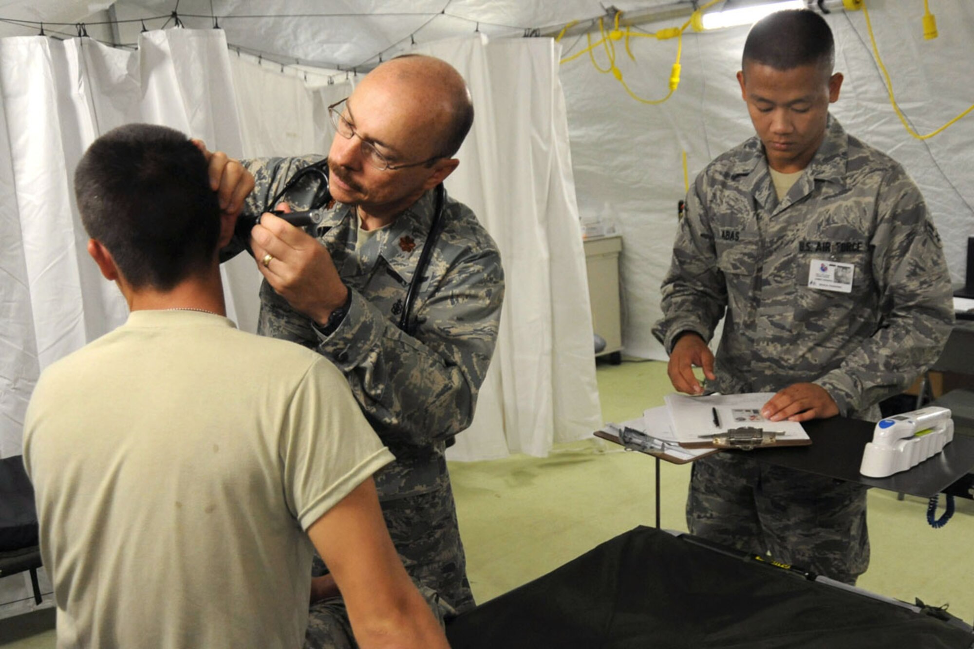 Maintaining a field hospital is just one of the behind-the-scenes services Airmen are providing at the 100th National Boy Scout Jamboree taking place at Fort A.P. Hill, Va.  Here, Maj. David De Lang, a registered nurse from Elmendorf Air Force Base, Alaska, examines a sick patient as Airman 1st Class Wilfredo Abas, from Randolph AFB, Texas, assists. (Department of Defense photo/Michael Tolzmann)