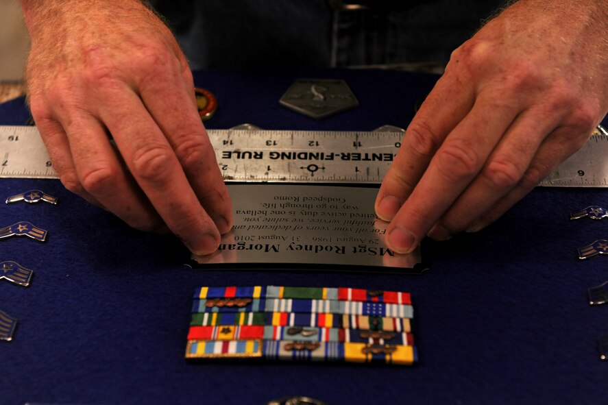 MOODY AIR FORCE BASE, Ga. -- Jim Connelly, Wood Shop supervisor, uses a ruler to level out the name plate and insignias during the final step of creating a shadow box here July 9. After everything is leveled out, a foam-covered blue cloth will become the backdrop for the shadow box. (U.S. Air Force photo by Airman 1st Class Joshua Green/RELEASED)