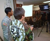 KUNSAN AIR BASE, Republic of Korea -- Specialist Sabrina Black, Armed Forces Network Korea at Kunsan, demonstrates using a teleprompter for a mock television report with a Republic of Korea student from Jik Island when his group visited here July 29. The students also toured the 8th Operations Support Squadron air traffic control tower during their visit. The visit was documented by both AFN and the Korean Forces Network. (Republic of Korea Air Force photo/Courtesy photo)