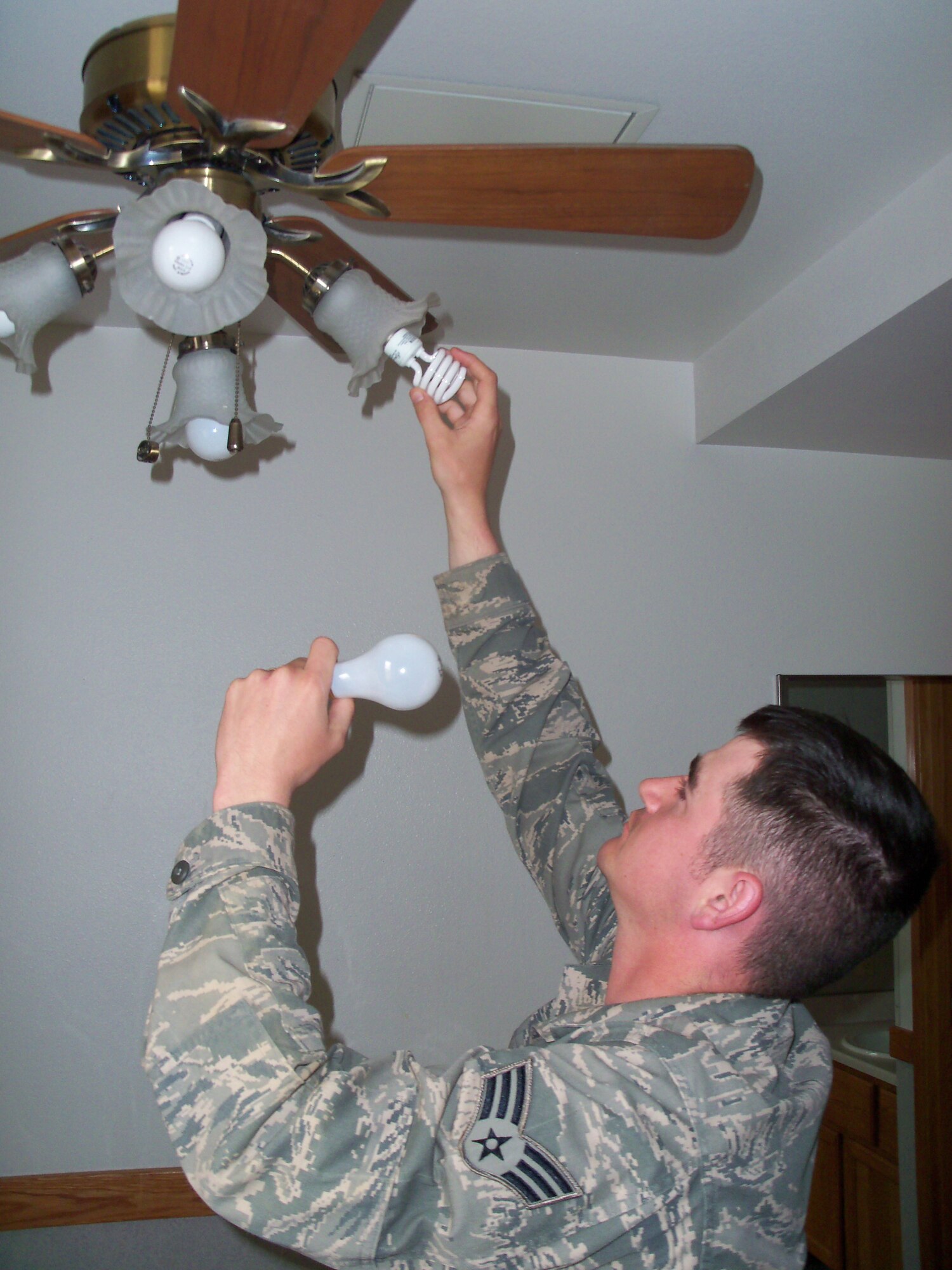 Senior Airman Brandon Harris-Miller changes out an incandescent bulb for a new compact florescent light bulb in a dormitory room as a part of Operation Change Out May 13, 2010, Eielson Air Force Base, Alaska . OCO?s objective is to promote energy awareness amongst military members by distributing free energy-efficient CFLs to base residents. Airman Harris-Miller is assigned to the 354th Civil Engineer Squadron. (Courtesy photo)