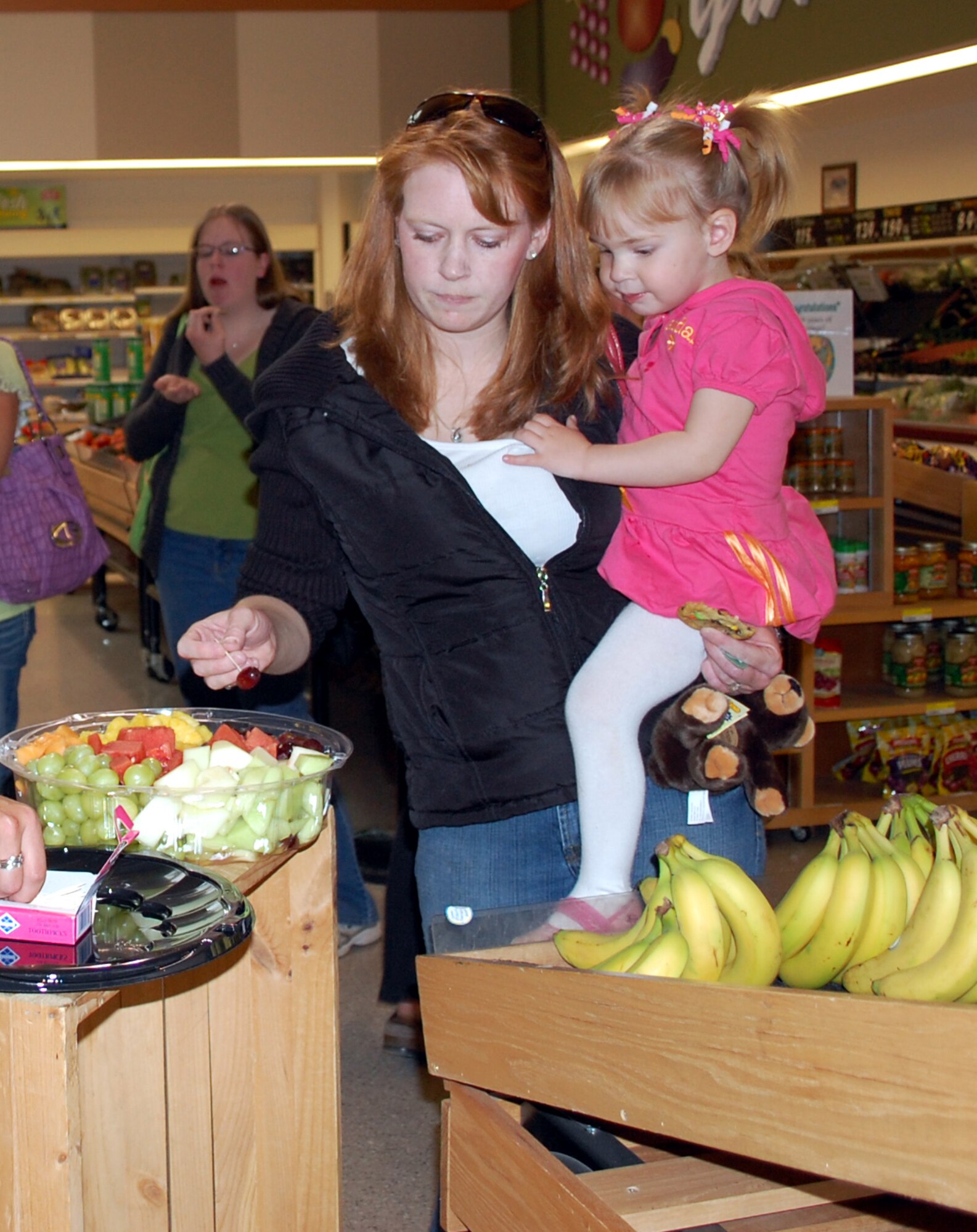 Amy Blado gets a grape for daughter, Kendall, before a produce briefing during Deployed Spouse's Night at the Commissary May 23. (U.S. Air Force photo/Valerie Mullett)