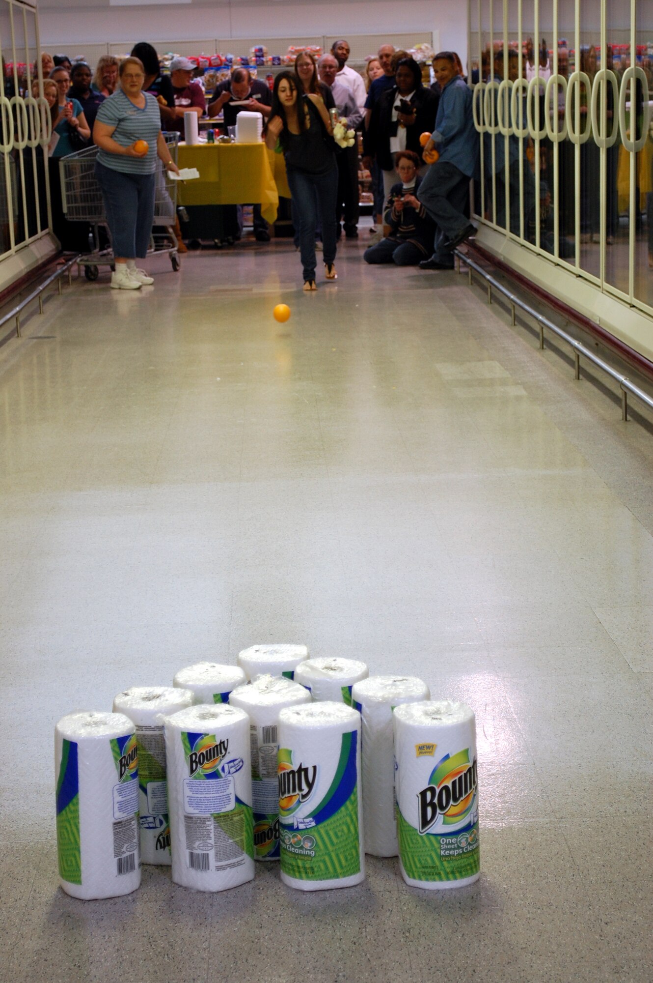 Malisa Vilella shows her form during the bowling with fruit game at the Commissary May 23 while other spouses and sponsors look on. (U.S. Air Force photo/Valerie Mullett)