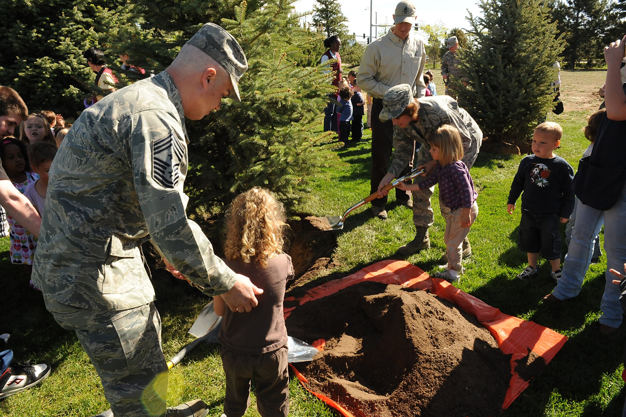 Chief Master Sgt. Robert Sealey, 21st Space Wing command chief, and Col. Kimerlee Conner, 21st Mission Support Group commander, get a little help from children at the Peterson Child Development Center, Building 1350, May 25, where three Colorado Blue Spruce trees were planted in honor of Arbor Day. Peterson Air Force Base was presented with the “Tree City USA” award from the National Arbor Day Foundation and the Colorado State Forest Service for the base’s dedication to planting and sustaining a healthy forestry program. (U.S. Air Force photo/Roberta McDonald)