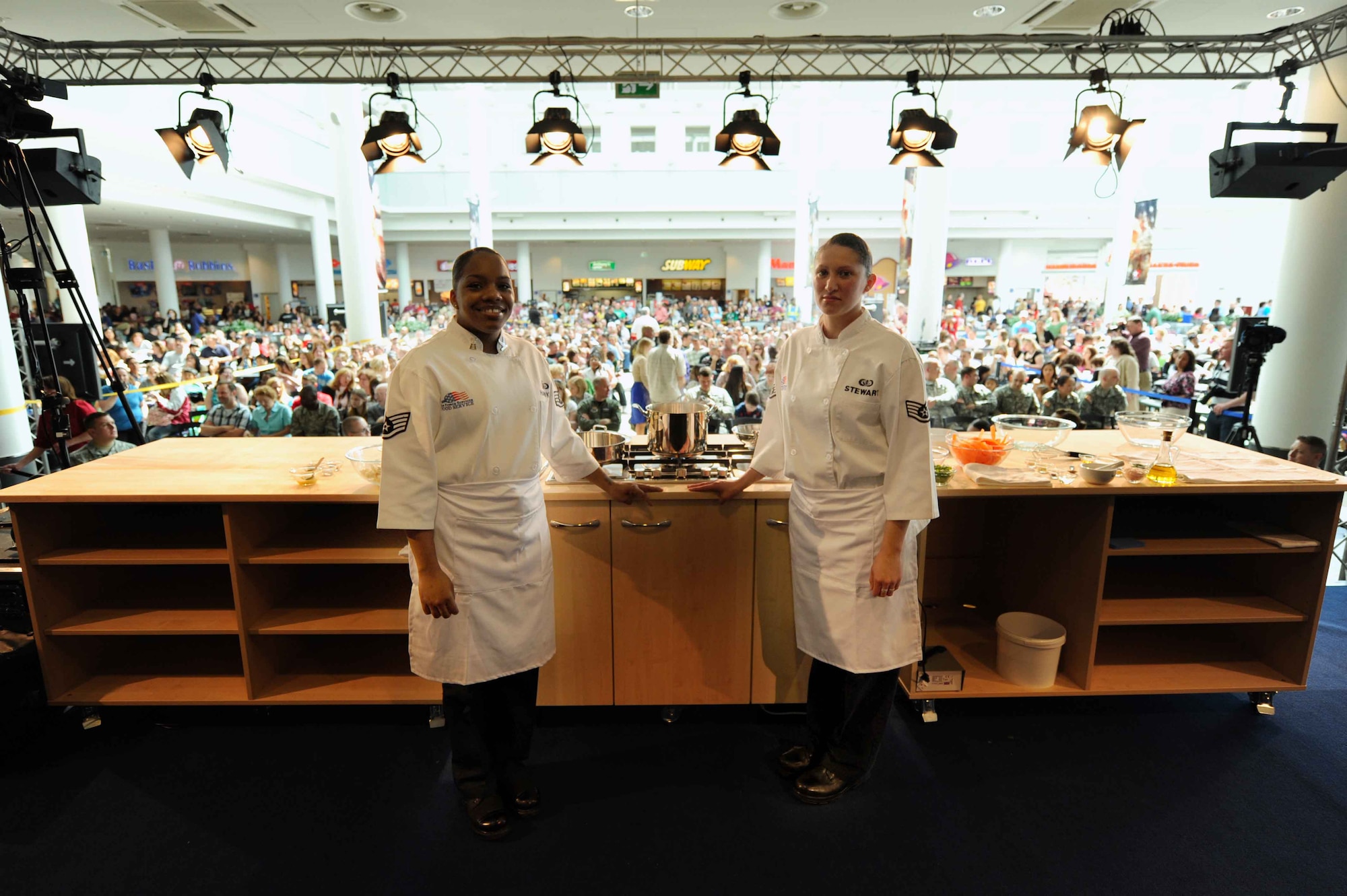 U.S. Air Force Staff Sgt's. Vilynthia Hawkins and Sheryl Stewart, 86th Services Squadron chef services specialists, pose for the camera prior to the Chef Emeril Lagasse cooking demonstration at the Kaiserslautern Military Community Center, Ramstein Air Base, Germany, May 29, 2010. The Sergeants were selected to accompany Celebrity Chef Emeril Lagasse during an hour long cooking demonstration at the KMCC. Chef Emeril was also on hand signing copies of his new book for over a thousand visitors. (U.S. Air Force photo by Staff Sgt. Stephen J. Otero)