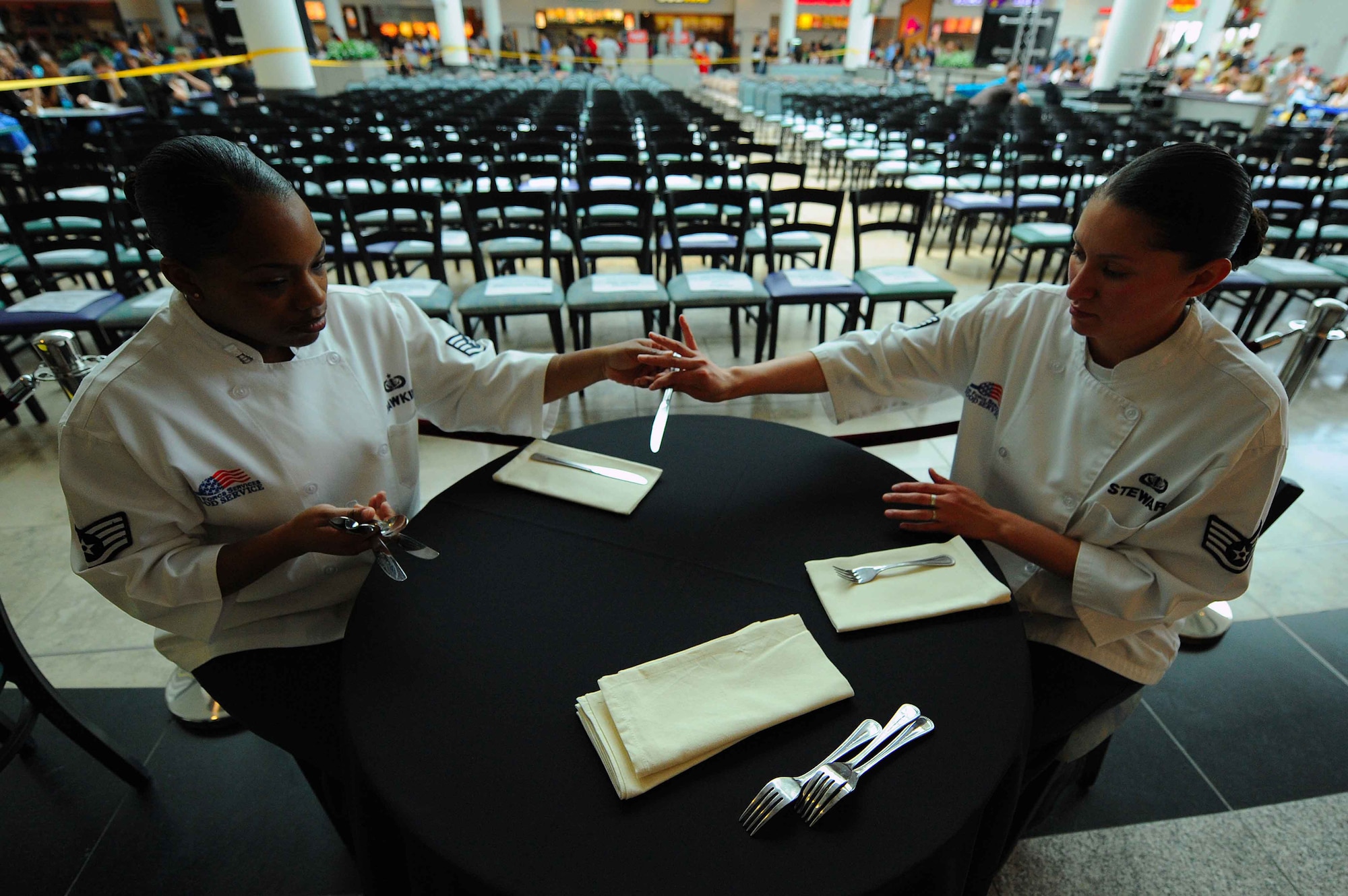 U.S. Air Force Staff Sgt's. Vilynthia Hawkins and Sheryl Stewart, 86th Services Squadron chef services specialists, prepare table settings for VIP guests prior to the Chef Emeril Lagasse cooking demonstration at the Kaiserslautern Military Community Center, Ramstein Air Base, Germany, May 29, 2010. Celebrity Chef Emeril Lagasse visited the KMCC to promote his new book along with providing a book signing and a full production cooking exhibition copies of his new book and performing an hour long cooking demonstration for over a thousand visitors. (U.S. Air Force photo by Staff Sgt. Stephen J. Otero)